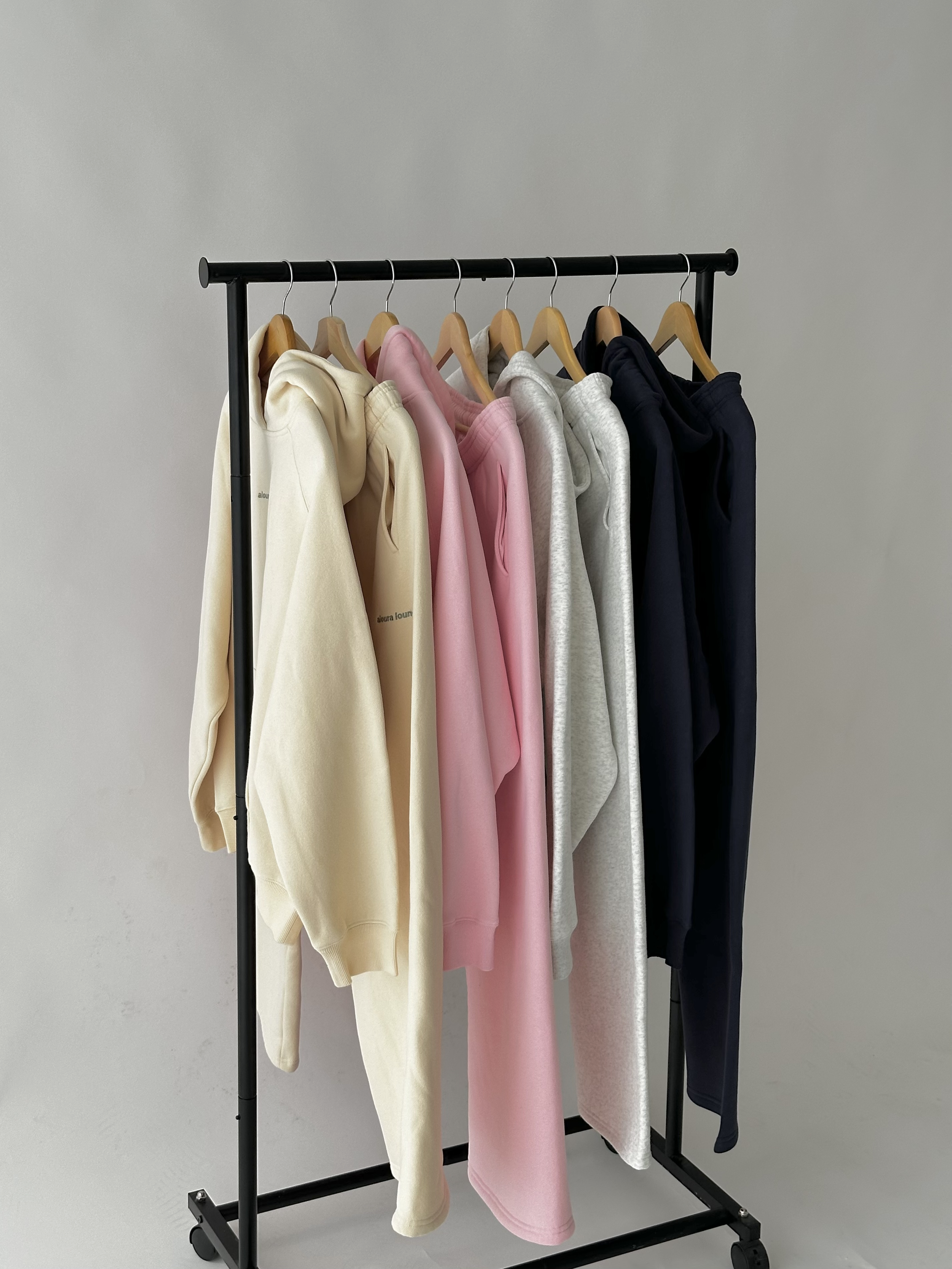 Clothing rack with hoodies in beige, pink, gray, and navy blue colors hanging on wooden hangers.