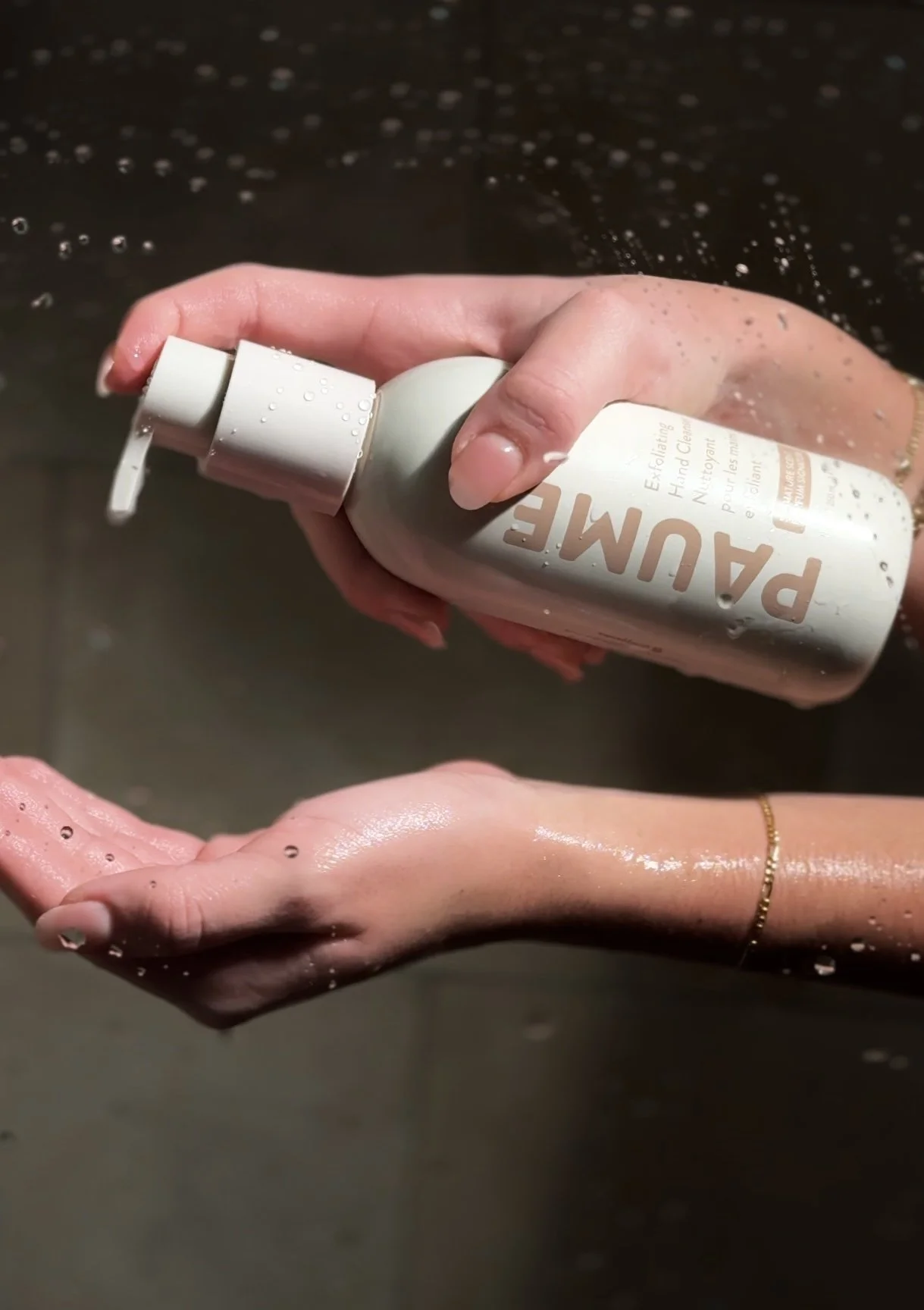 Person holding a bottle of hand sanitizer under running water in a sink