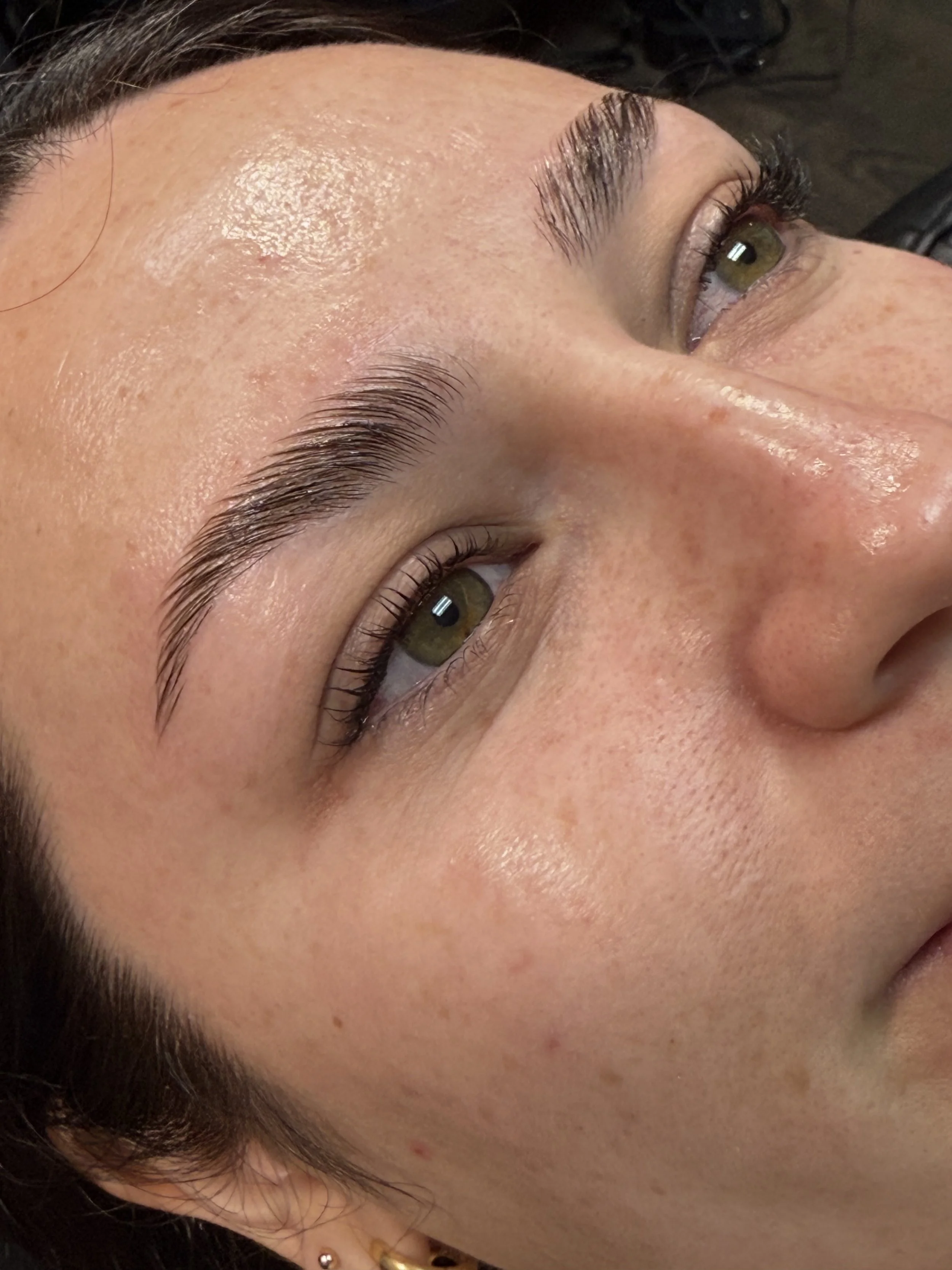 Close-up of a woman's face showing her eyebrows, nose, and eyes with natural makeup and clear skin.