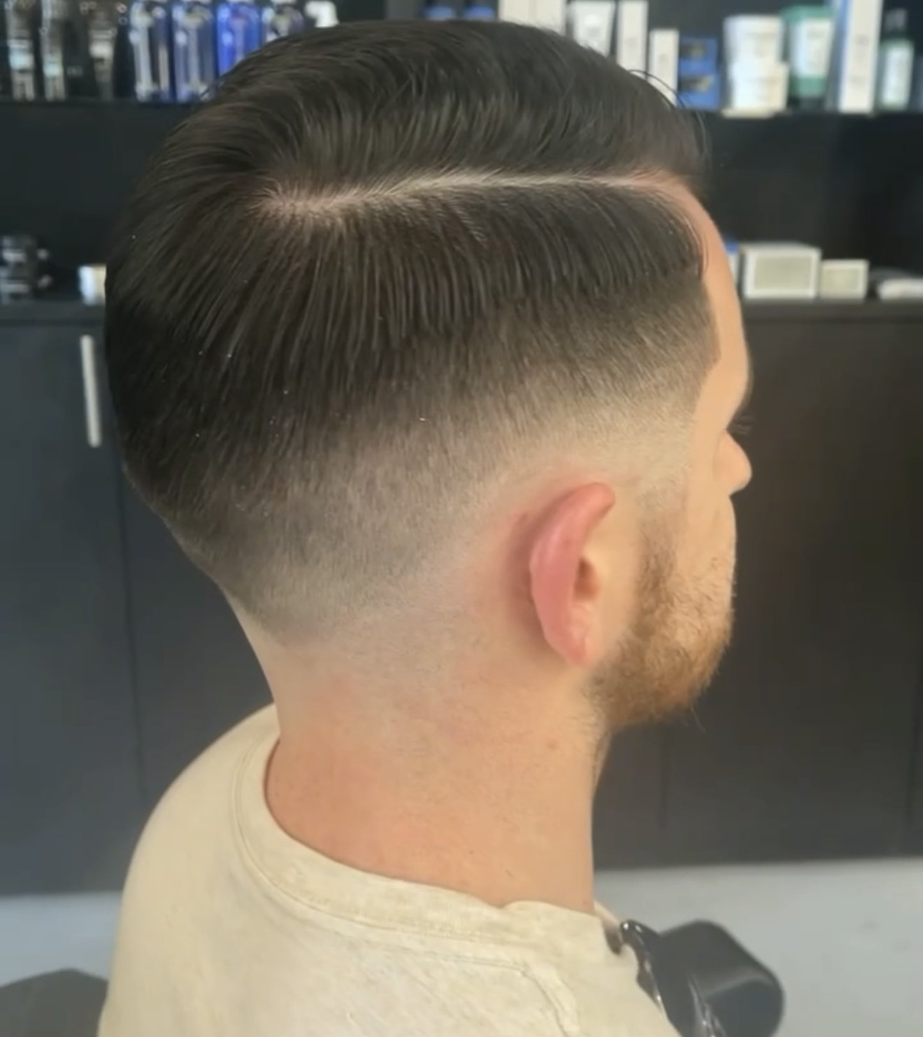Side view of a man with a short, faded haircut, sitting in a salon or barbershop.