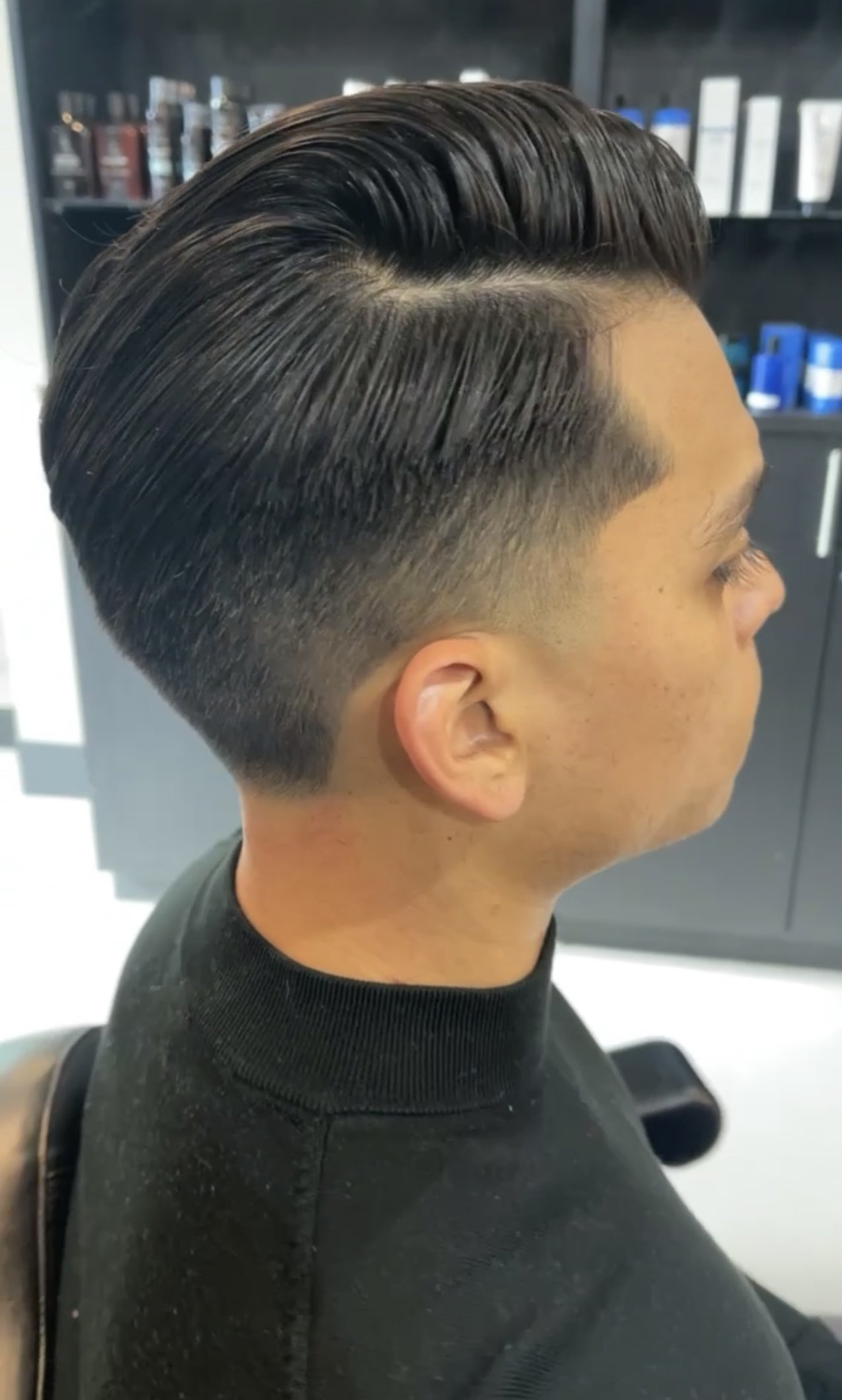 Side view of a man with a modern slicked-back hairstyle, featuring faded sides and a neatly styled top.