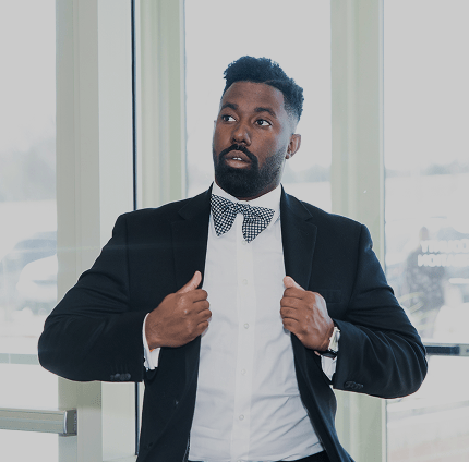 Man in a suit adjusting his jacket indoors with large windows in the background.