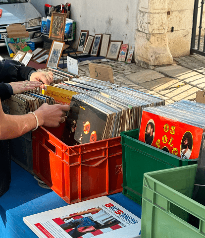 Outdoor record stall with vinyl records in plastic crates on a blue table, and framed pictures leaning against the wall.