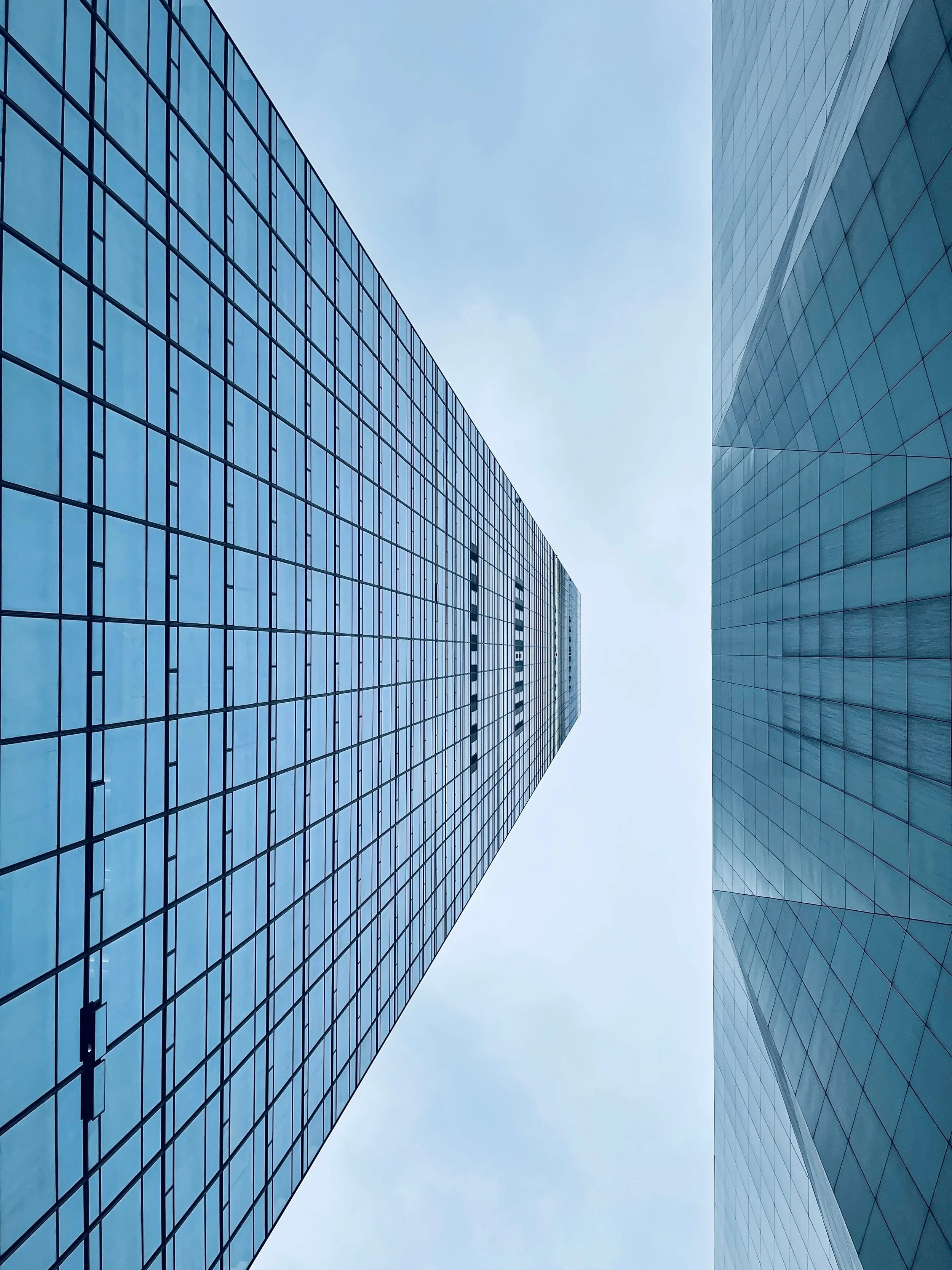 Looking up at two tall glass skyscrapers with reflective windows, converging towards the sky.