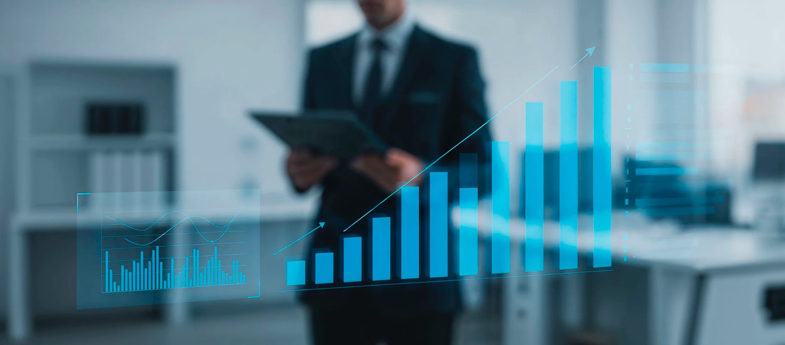 A businessman in a suit holding a tablet with a digital overlay of rising bar and line graphs in an office setting.