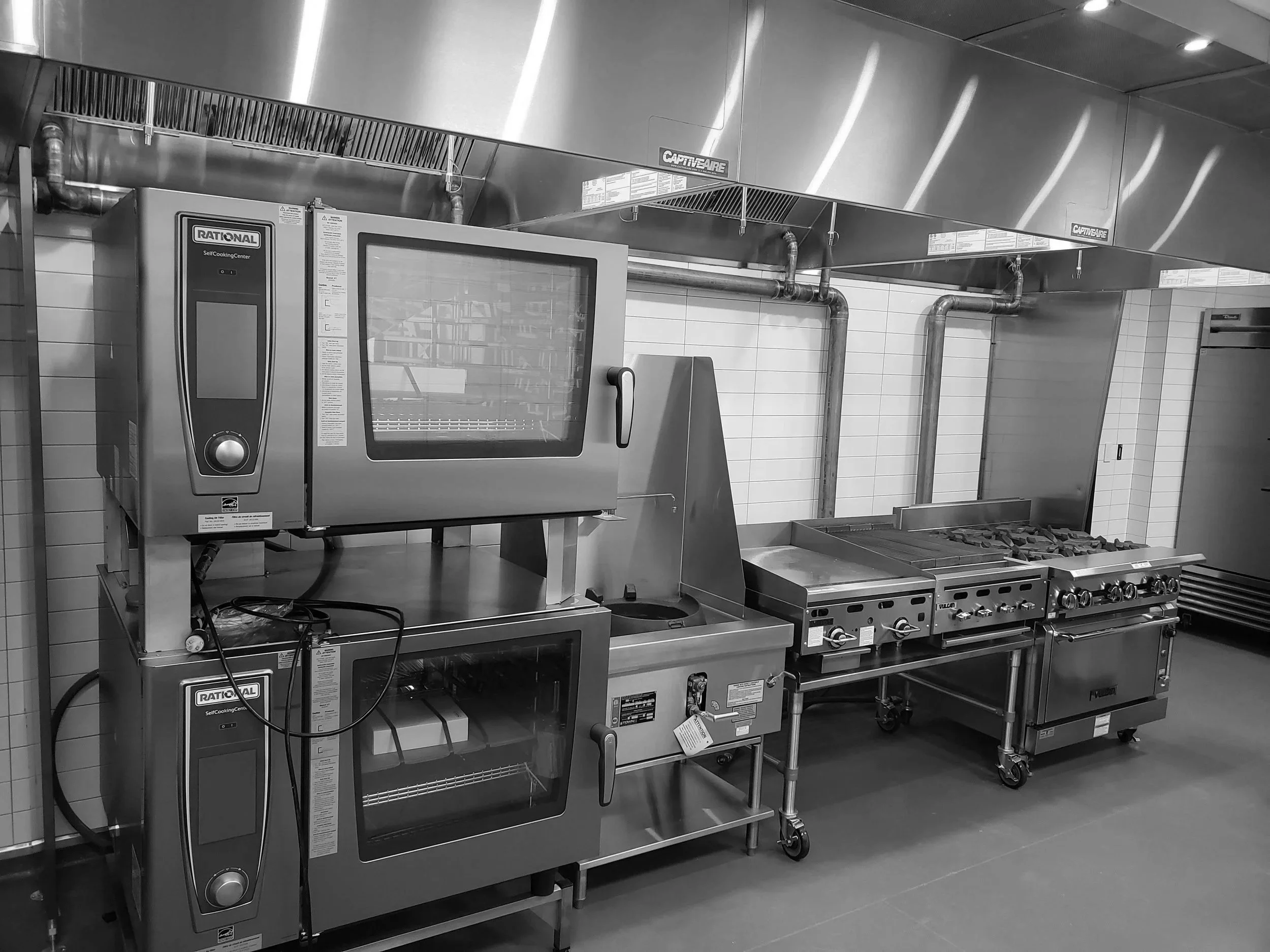 Commercial kitchen with stainless steel appliances including two ovens, a microwave, a fryer, and a stove with burners.