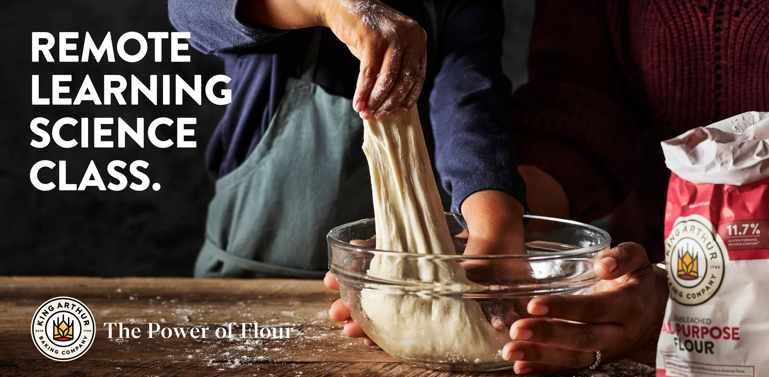 Child stretching dough in a glass bowl during a baking science class at King Arthur Flour. A bag of flour is on the right.