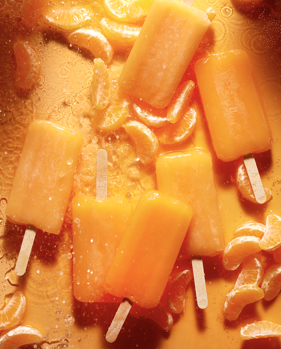 Close-up of orange popsicles and orange slices in a liquid, with scattered orange segments.