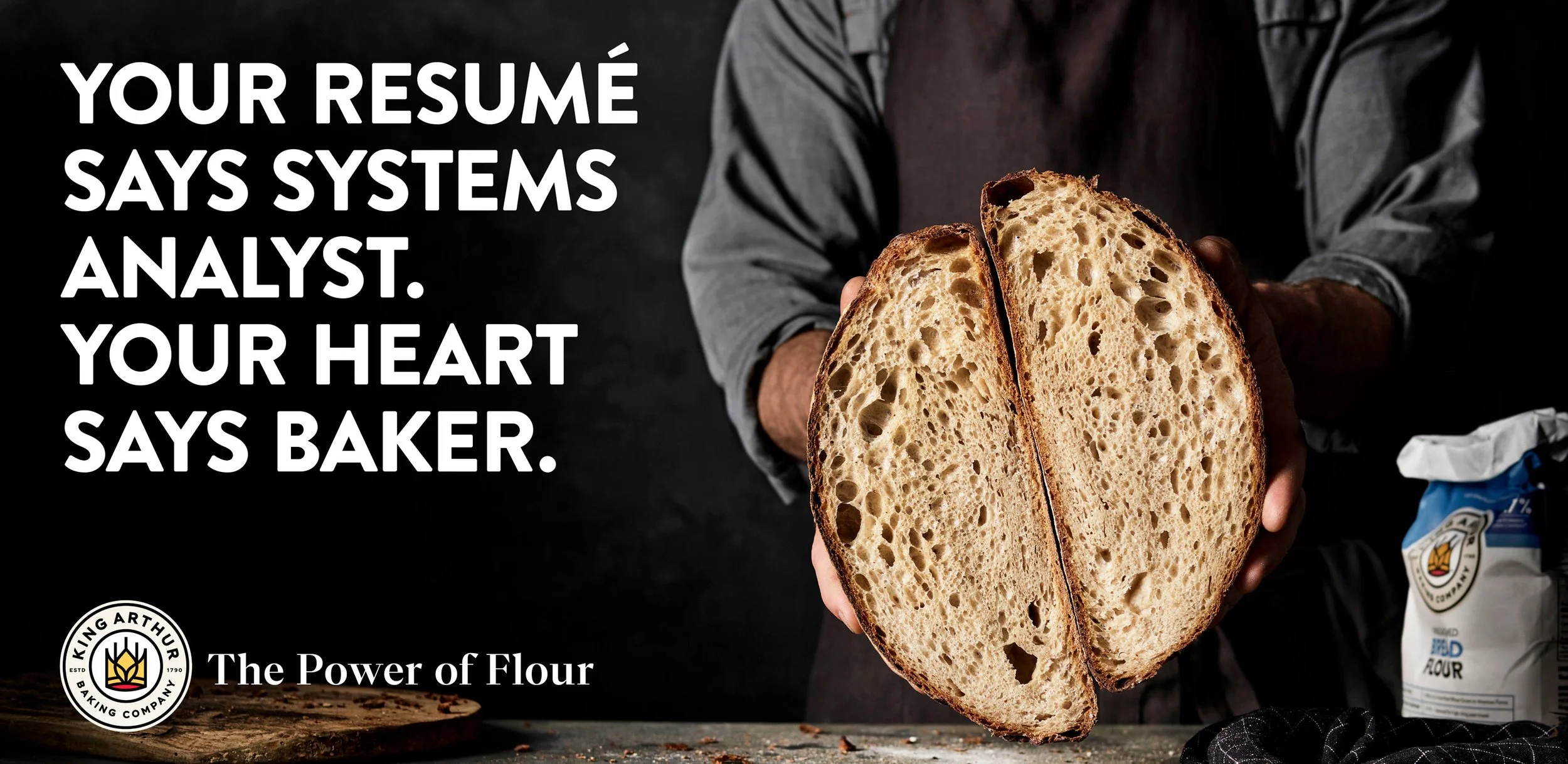 Man holding a halved loaf of bread in front of a bag of flour with office background