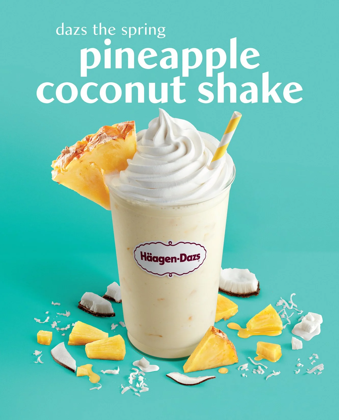 A vanilla pineapple coconut milkshake with whipped cream, a pineapple slice, and a striped straw, against a turquoise background with scattered pineapple pieces and coconut flakes.