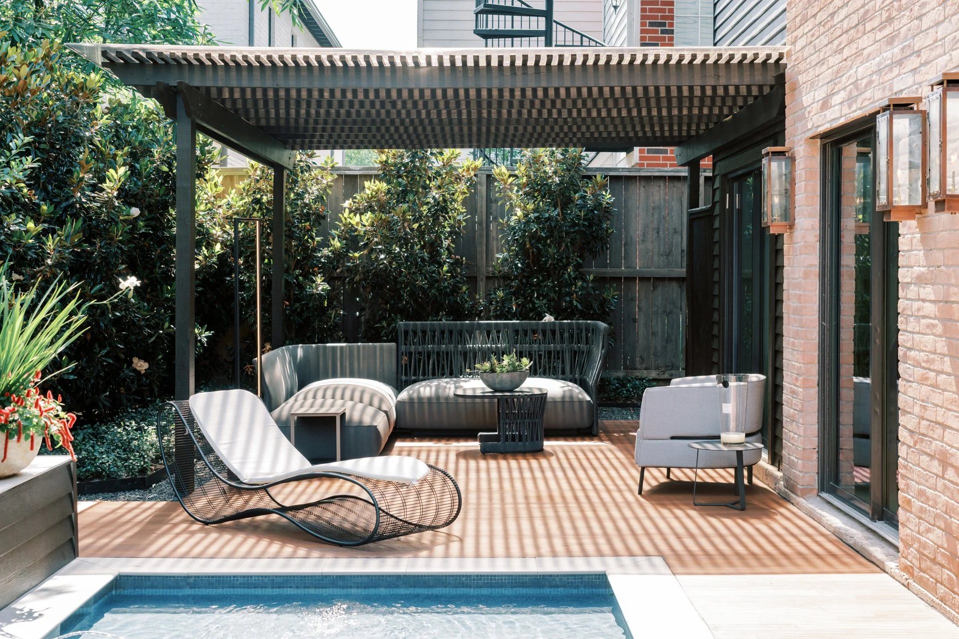 Outdoor patio with pergola, modern furniture, plants, and adjacent pool.