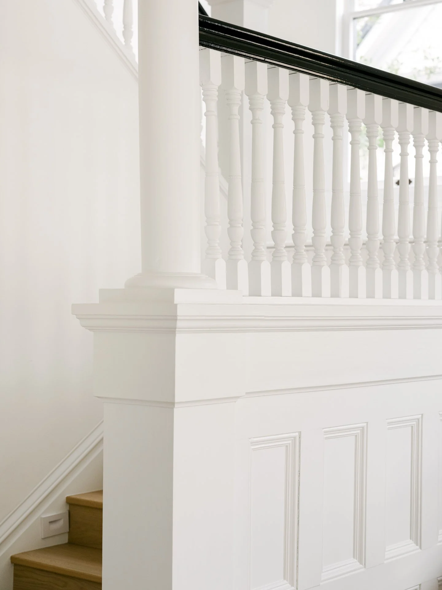 Close-up of a white wooden staircase featuring decorative spindles and a black handrail.