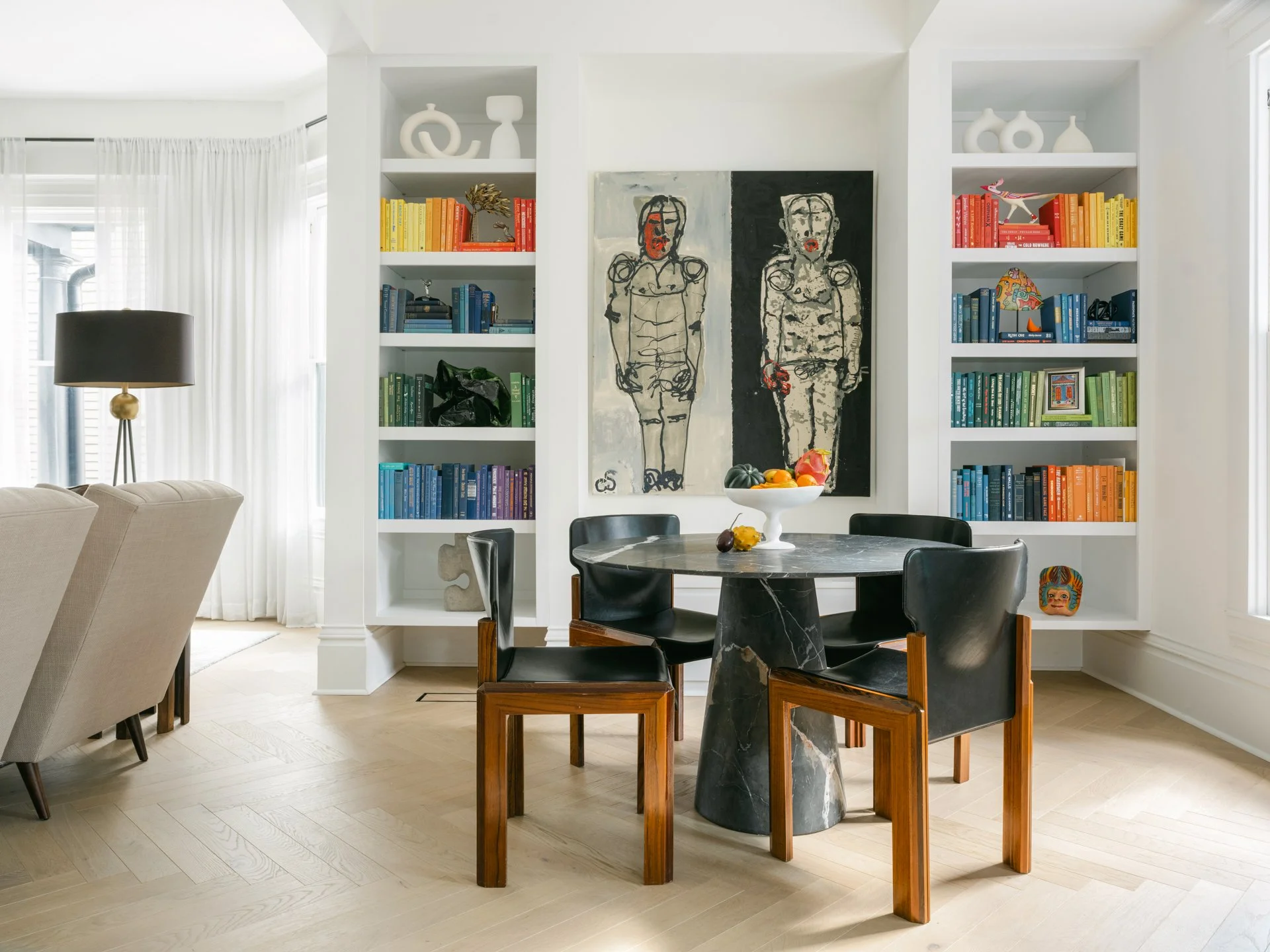 Modern interior with black dining table, art on wall, and bookshelves with rainbow-organized books.