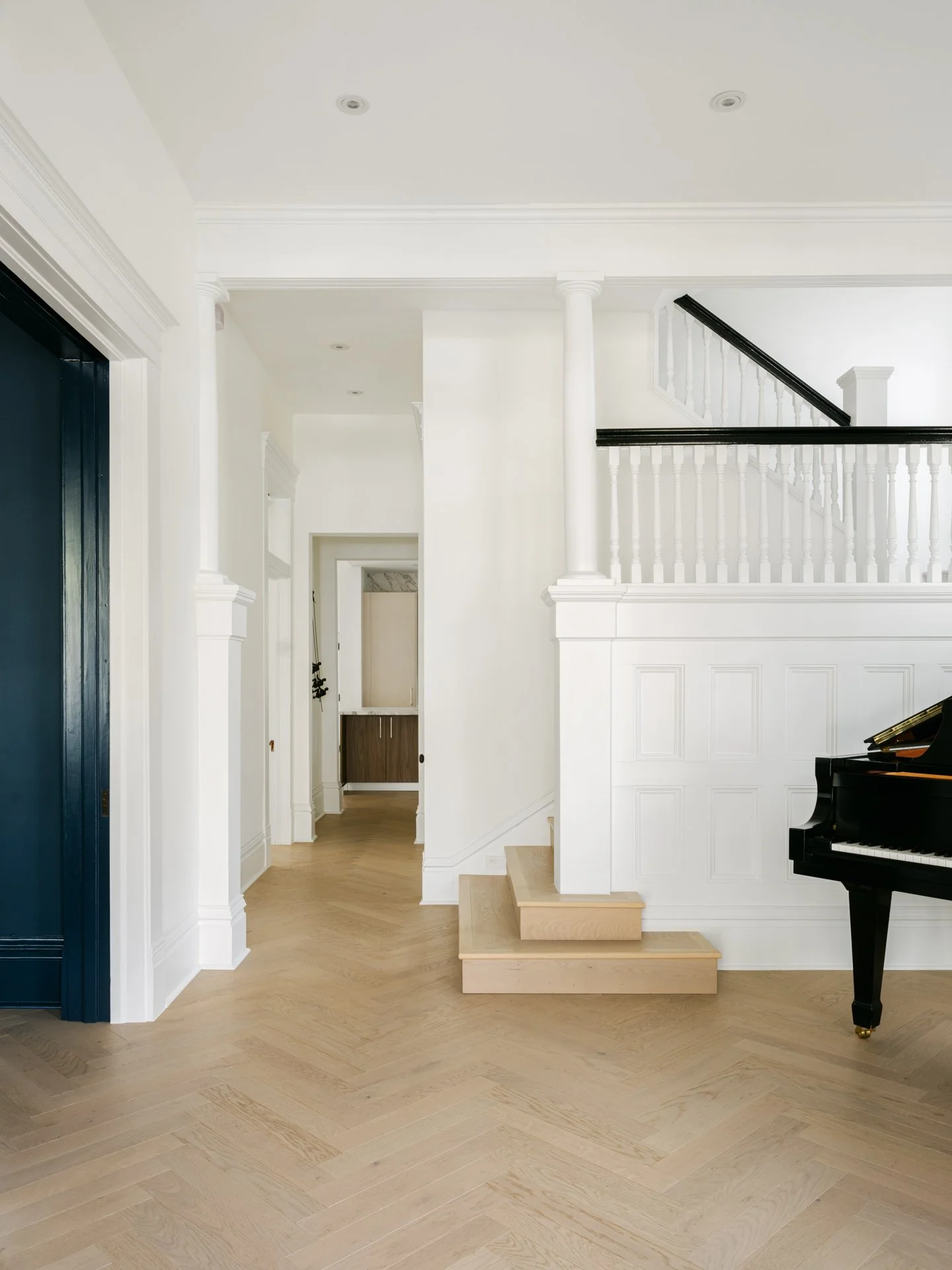 Minimalist interior with white walls, wooden floor, black grand piano, and staircase.