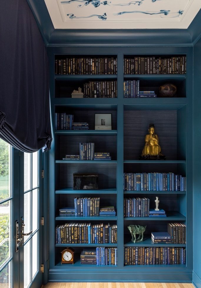 Blue bookshelf with books, golden Buddha statue, small sculptures, French doors, and decorative ceiling.