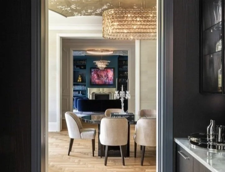 Elegant modern dining room and living area with chandelier, round table, upholstered chairs, and art on wall.