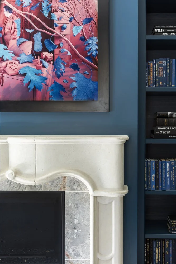 interior decor featuring a colorful painting, white fireplace, and bookshelf with books