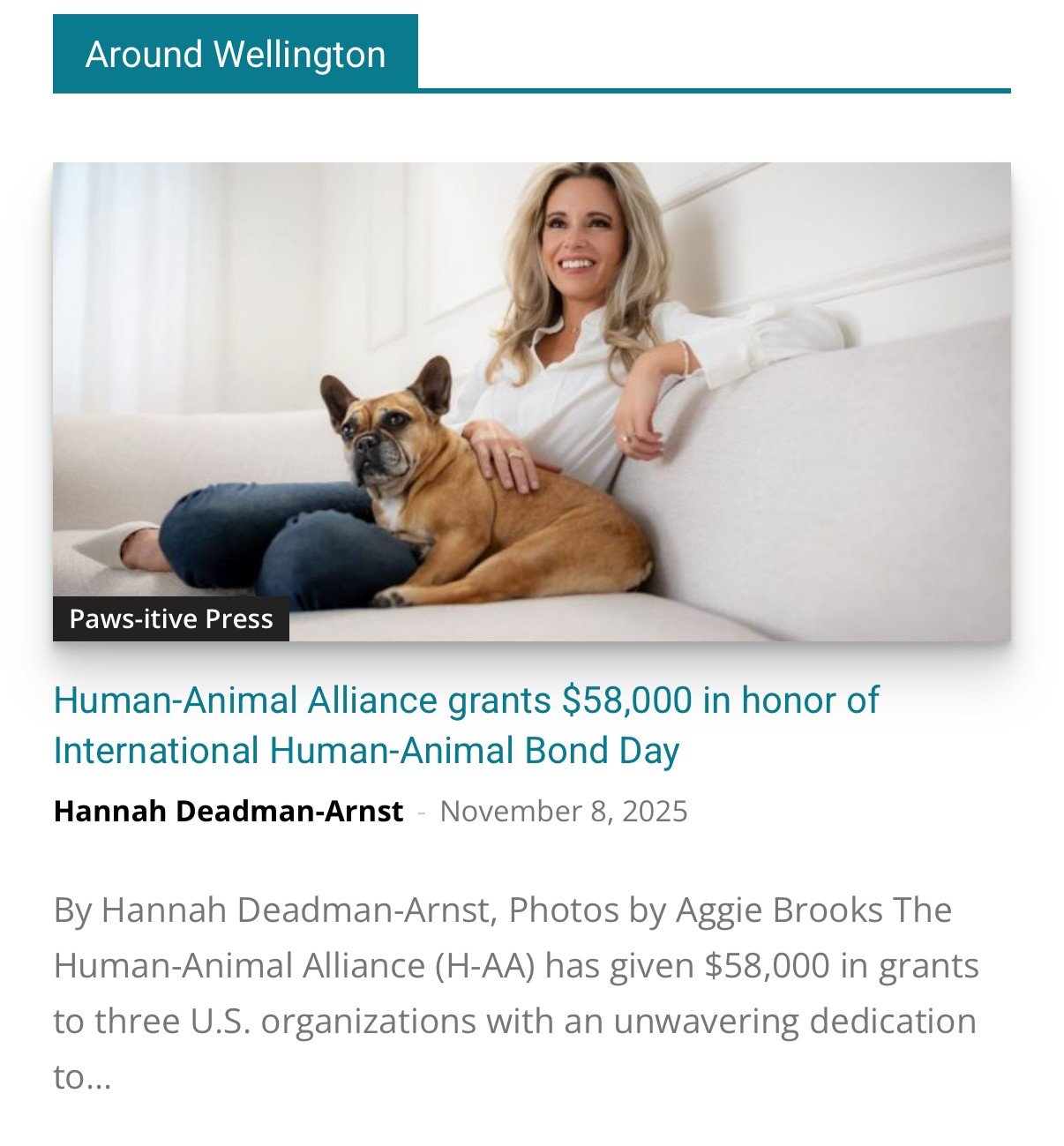 A woman with blonde hair sitting on a white couch, smiling, with a brown and white dog resting on her lap. The background is a bright, airy room with white curtains.