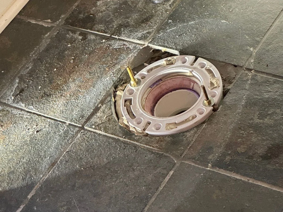 Exposed toilet drain and flange providing access for residential sewer cleaning.
