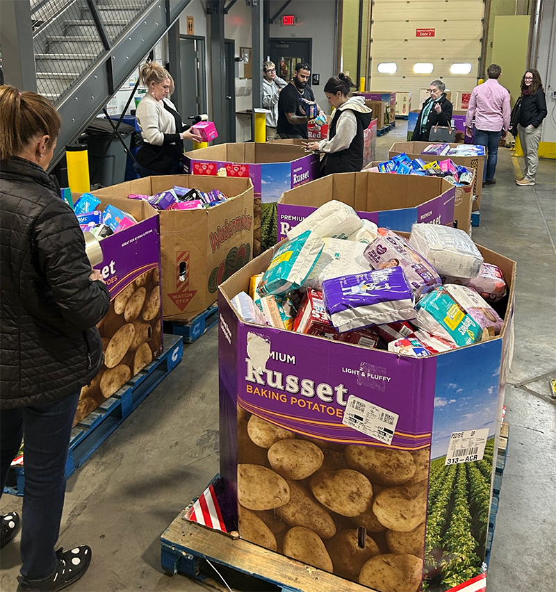 People volunteering at a food bank, sorting and packing boxes of supplies in a warehouse.