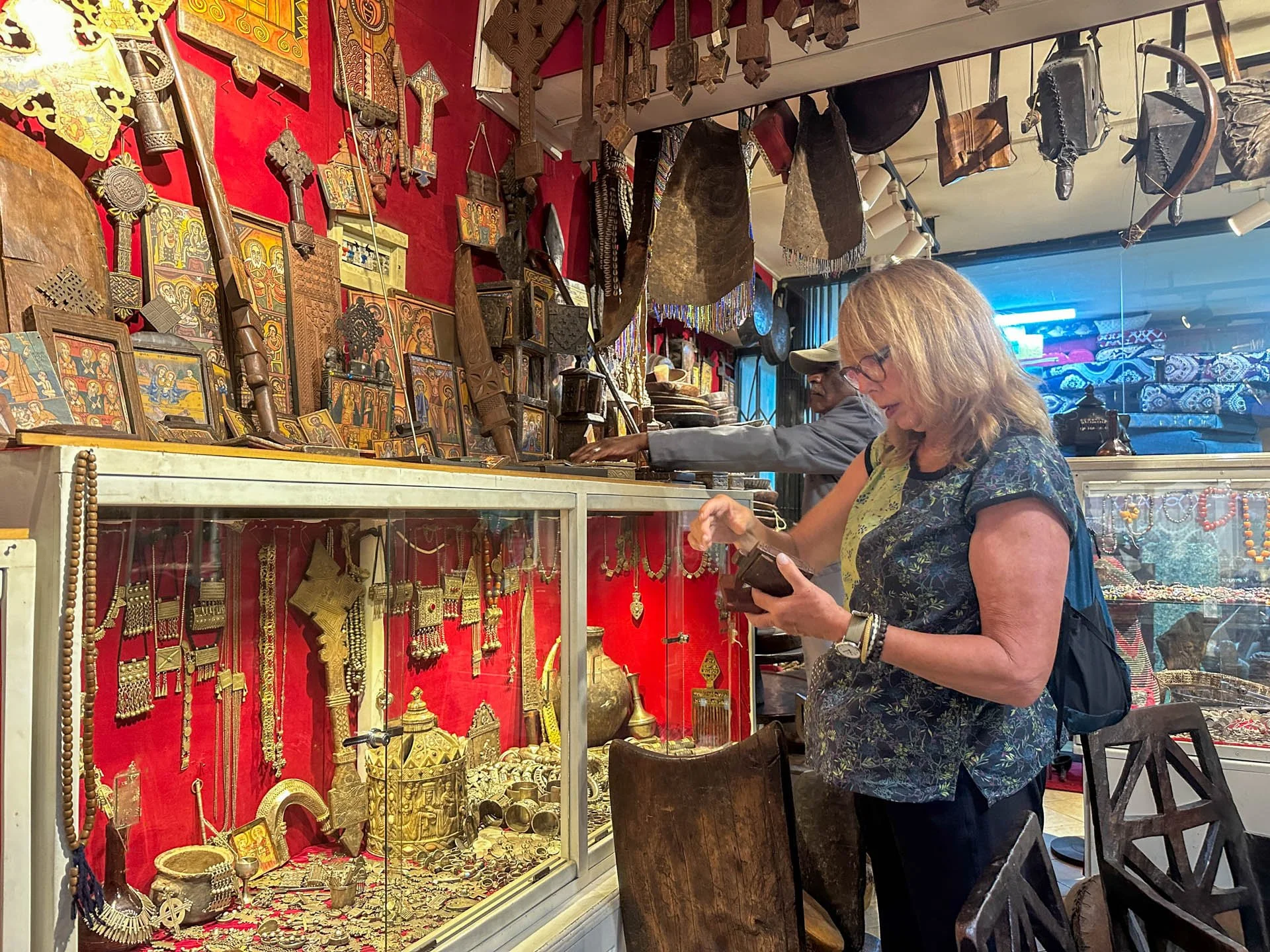 Caravan Gallery in La Conner, WA - Owner Linda shopping for jewelry and artifacts at an antique shop in Ethiopia with red walls decorated with gold and wooden items.