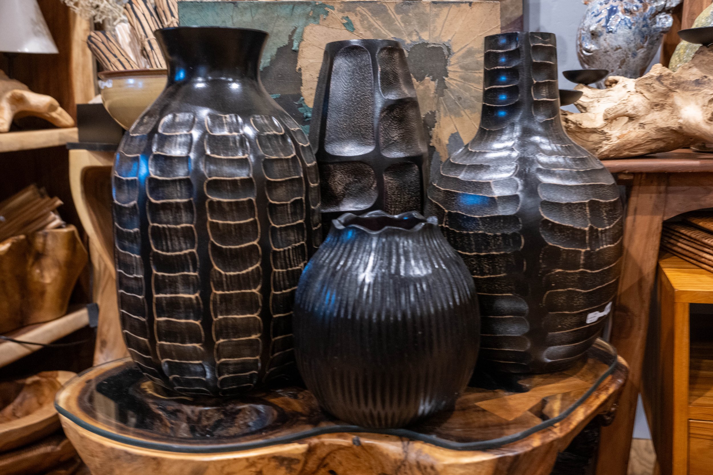 Caravan Gallery in La Conner, WA - A collection of black wood vases with textured, geometric patterns displayed on a wooden table in a rustic store.
