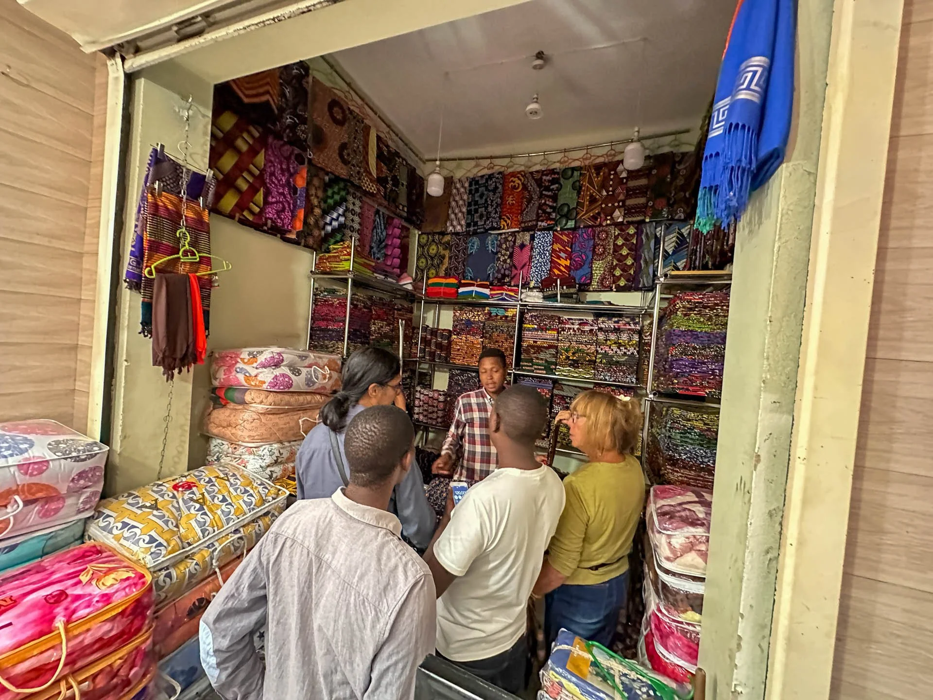 Caravan Gallery in La Conner, WA - Owner Linda Banaszak shopping in a fabric store with shelves full of colorful textiles and traditional cloths In Arusha Tanzania