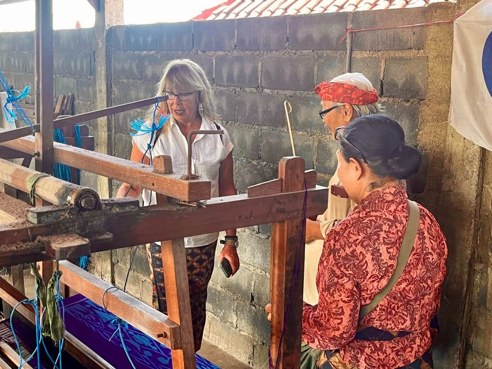 Three women engaging in traditional textile weaving with a loom in a rustic setting.