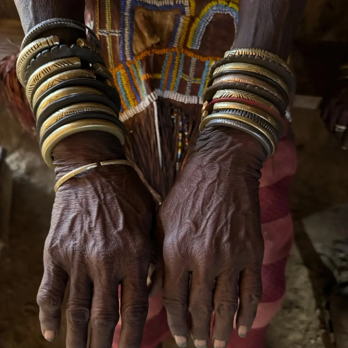 Caravan Gallery in La Conner, WA - Close-up of Dakoga Woman's hands, adorned with multiple colorful beaded and metal bracelets, in front of their traditional beaded garment.