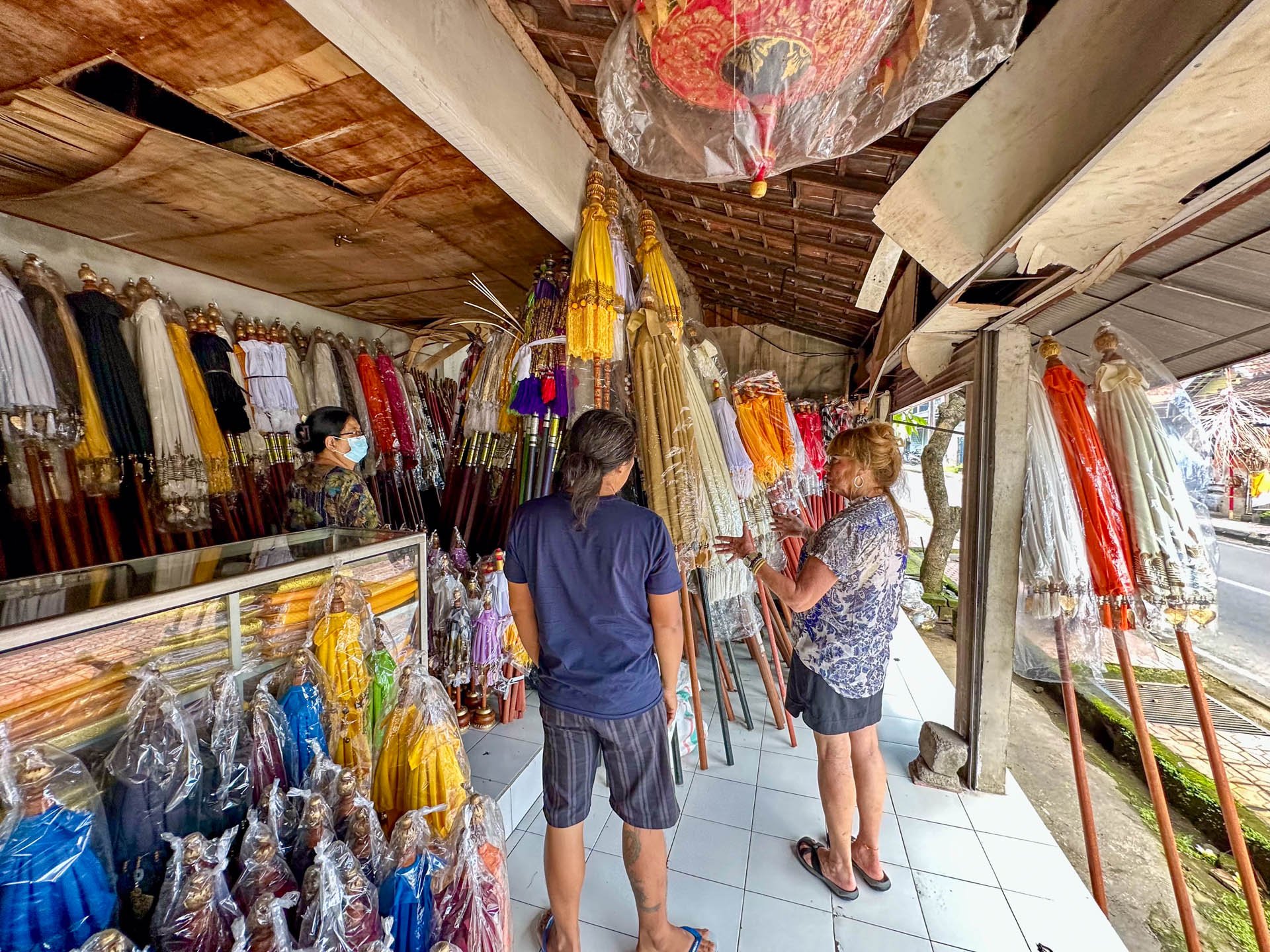 Caravan Gallery in La Conner, WA - Owner Linda shopping for umbrellas and parasols outside a shop in Bali. With umbrellas displayed on racks and leaning against the wall.