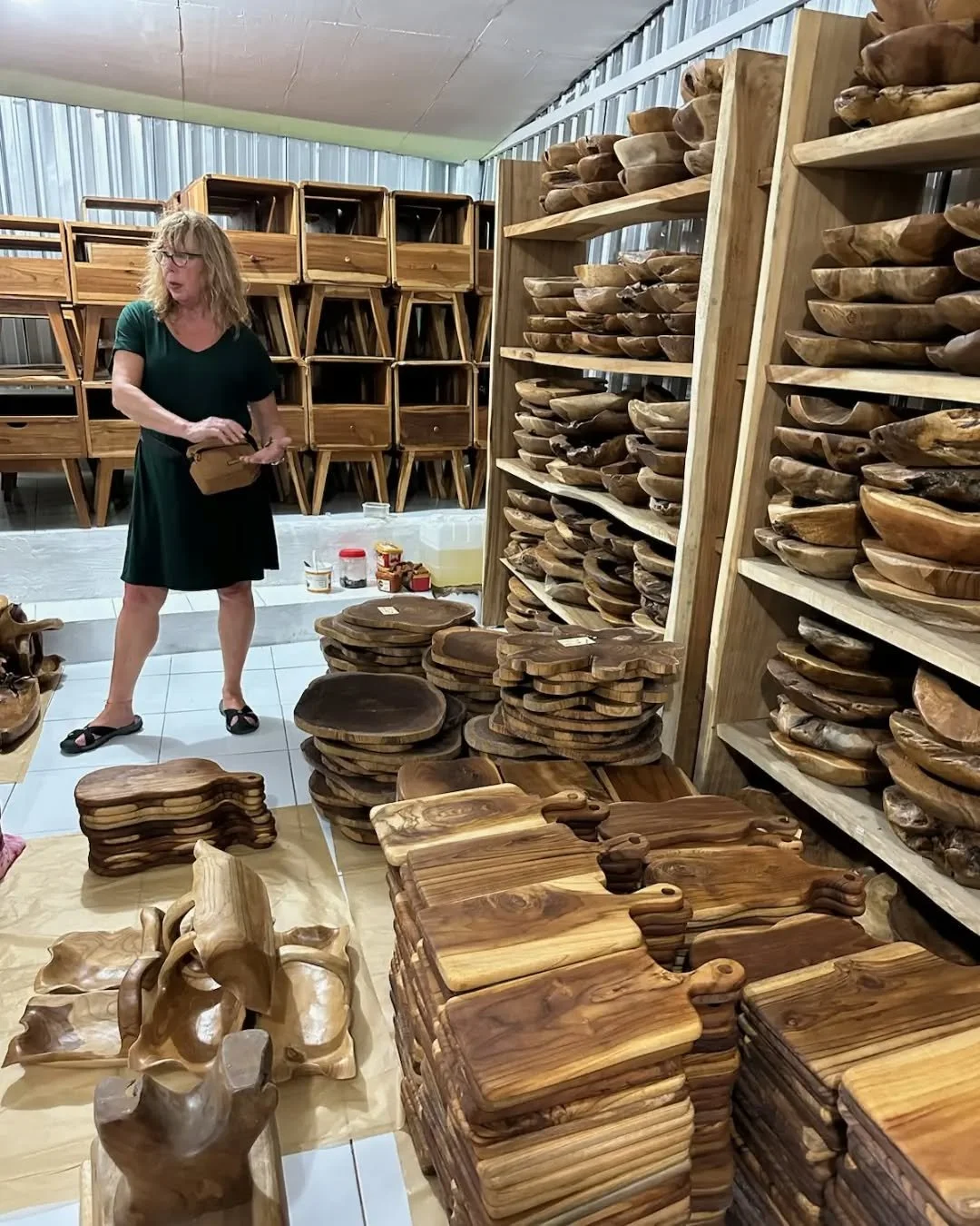 Caravan Gallery in La Conner, WA - Owner Linda shopping for wooden bowls and cutting boards, some stacked on shelves and others arranged on the floor in Bali. 