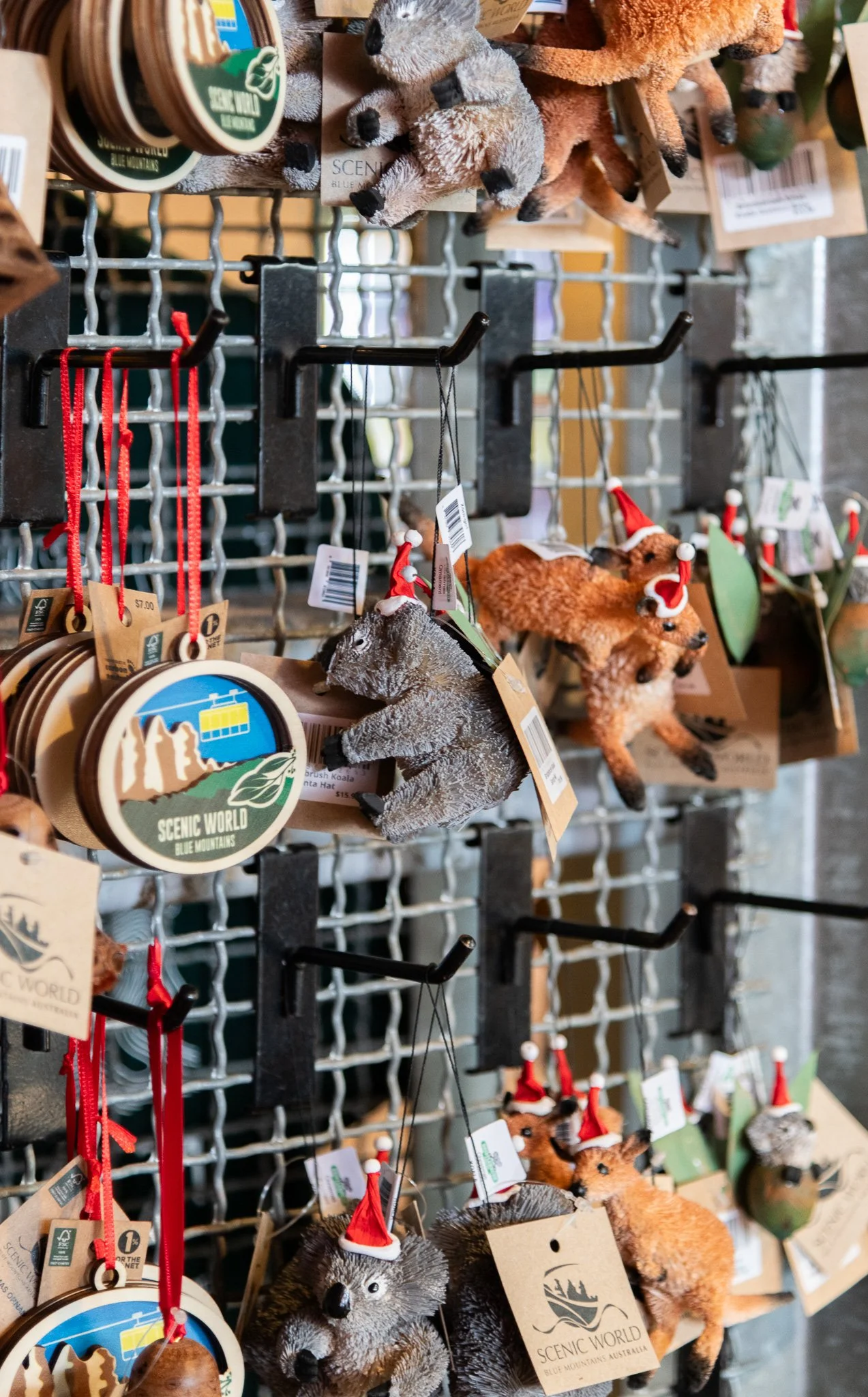 Assorted Christmas-themed plush animal ornaments, including koalas, possums, and raccoons, hanging on a display rack with tags and some wearing Santa hats.