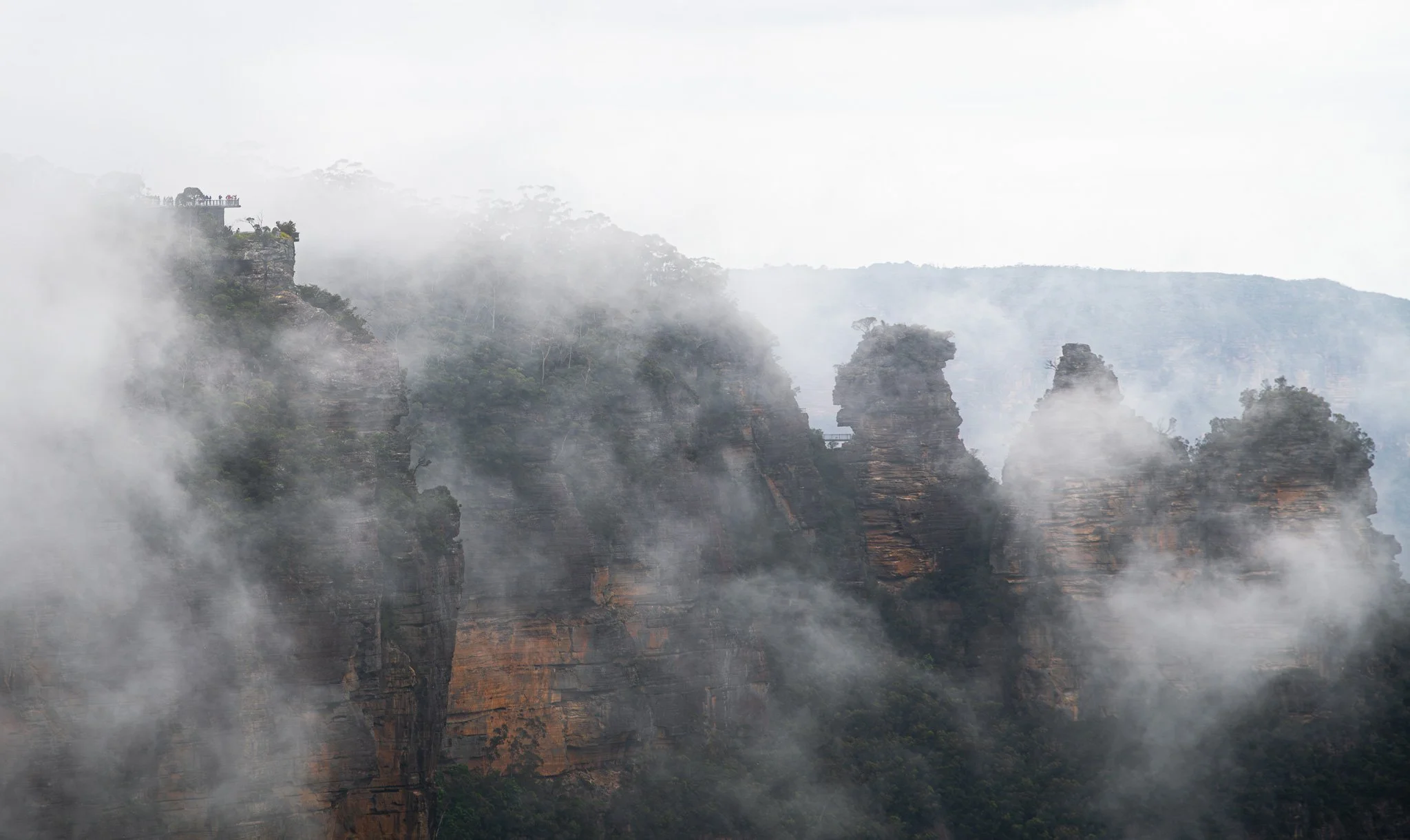Misty mountain landscape with steep cliffs and lush green trees, partially obscured by fog.