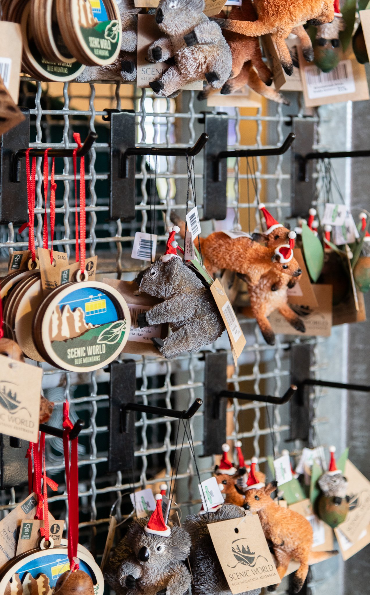 Display of plush animals and souvenirs featuring koalas and other wildlife, some wearing Santa hats, hanging on hooks in a retail store.