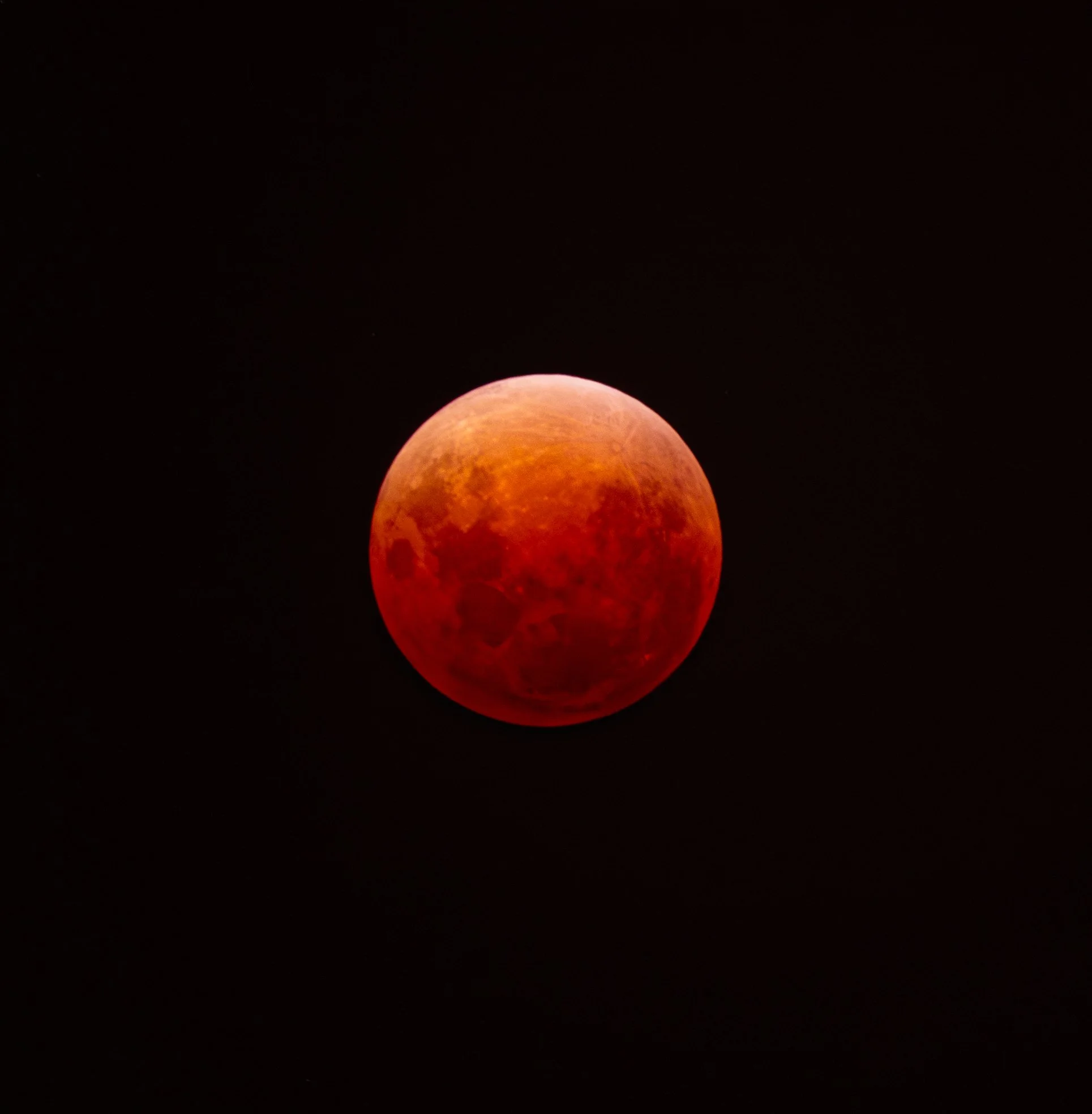 A reddish moon or planet against a dark night sky.