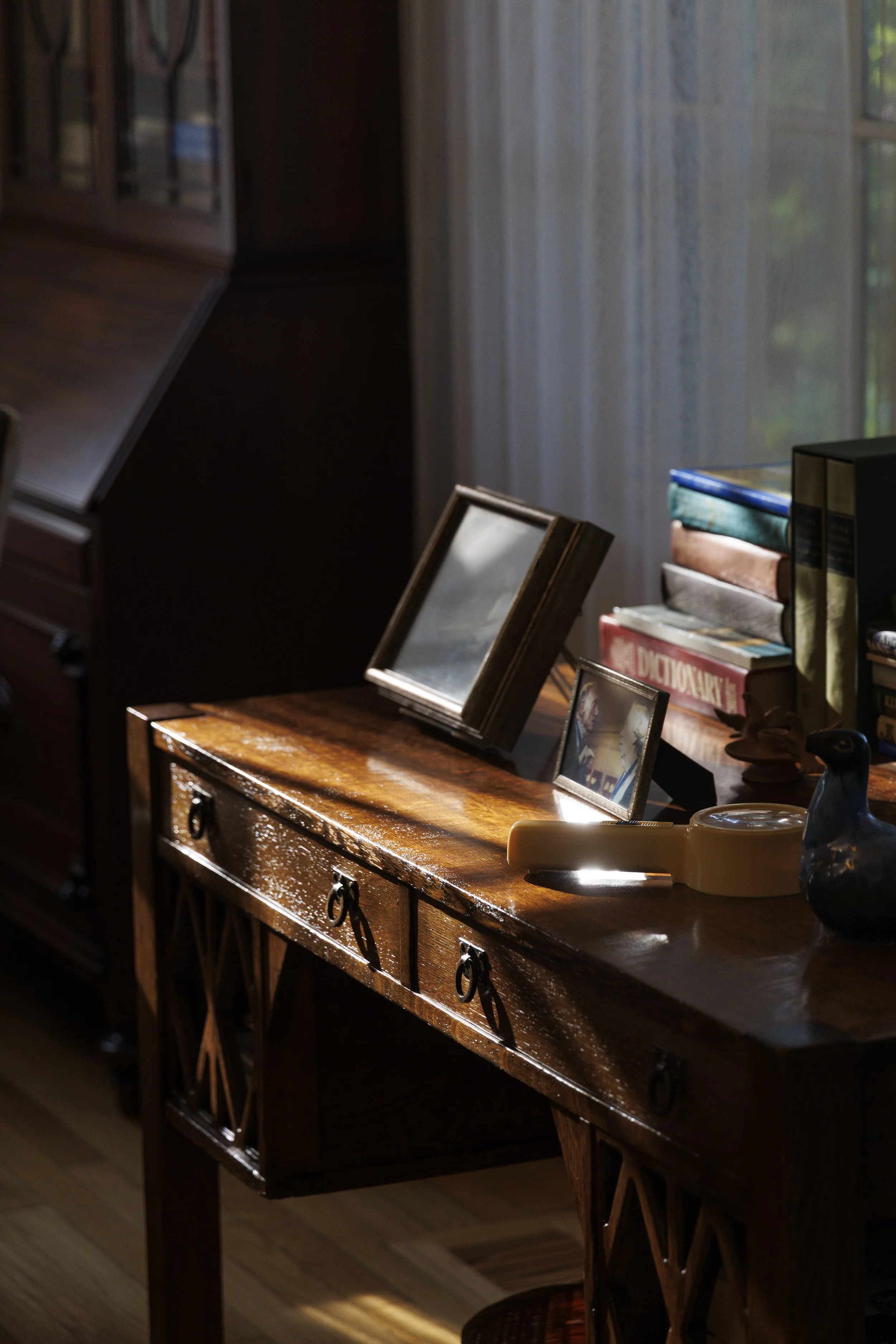 Wooden desk with photo frames, books, and decorative items illuminated by sunlight near a window.