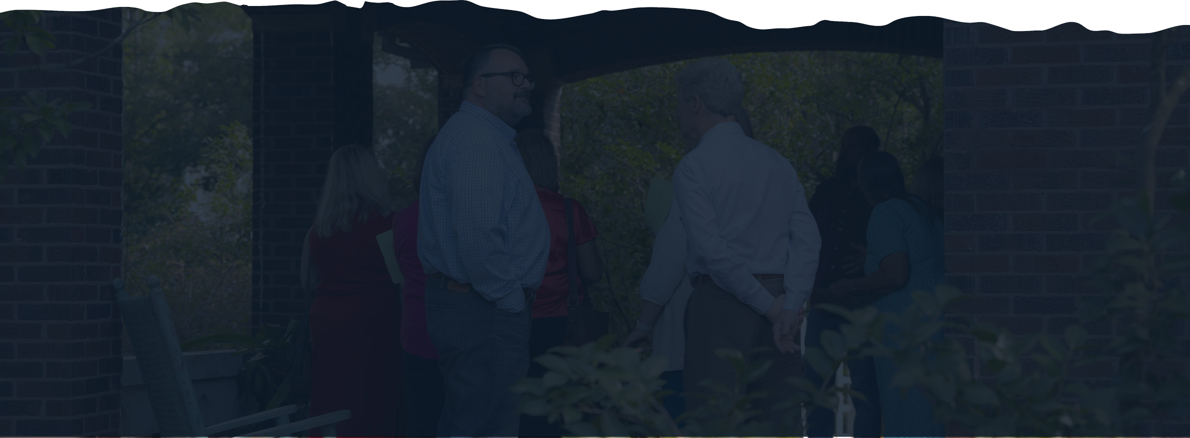 Group of people gathered outdoors near a brick structure, engaged in conversation.