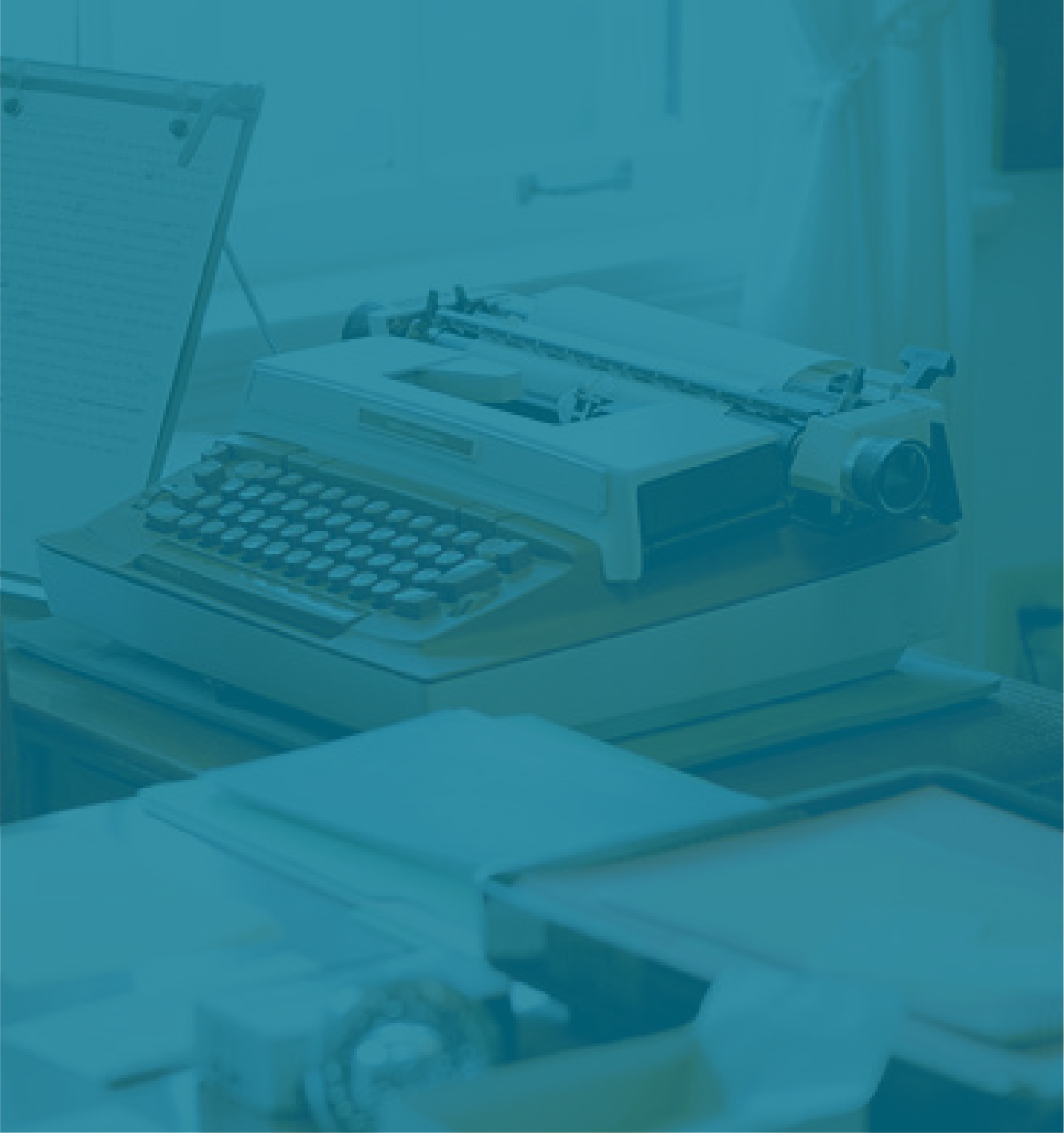 An old-fashioned typewriter on a desk with notebooks and a laptop nearby.