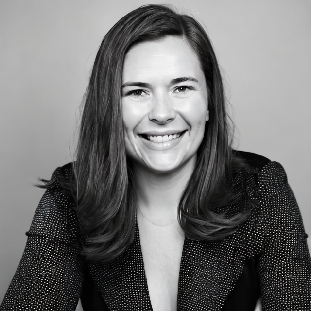 Black and white portrait of a smiling woman with shoulder-length hair, wearing a dotted blazer, against a plain background.