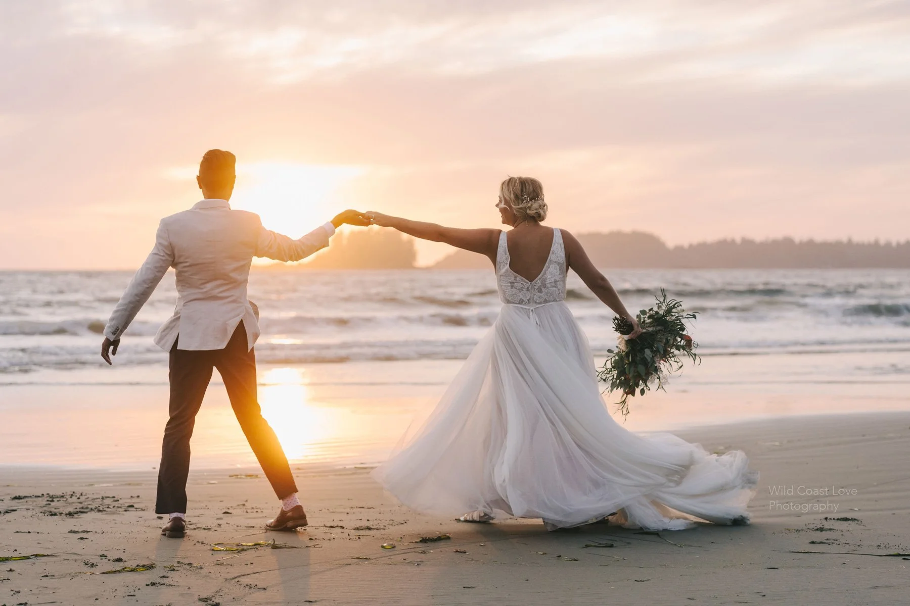 A bride and groom holding hands while walking on the beach at sunset, with the bride holding a bouquet of flowers.