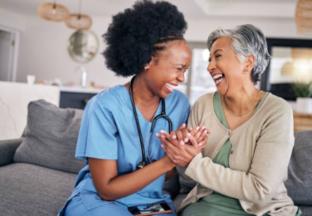 A nurse in blue scrubs talking with an elderly man holding a cane in a bright room.