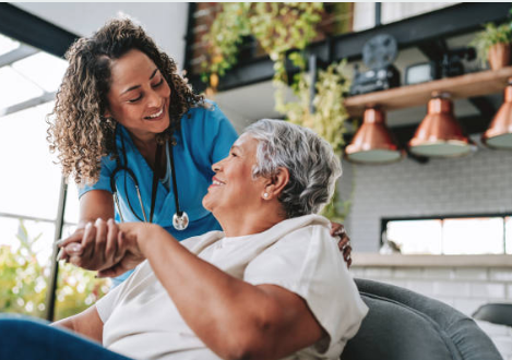 A young woman pouring tea for an elderly man who is about to eat toast with jam, sitting at a kitchen table with bread, bananas, apples, and a jar of jam.