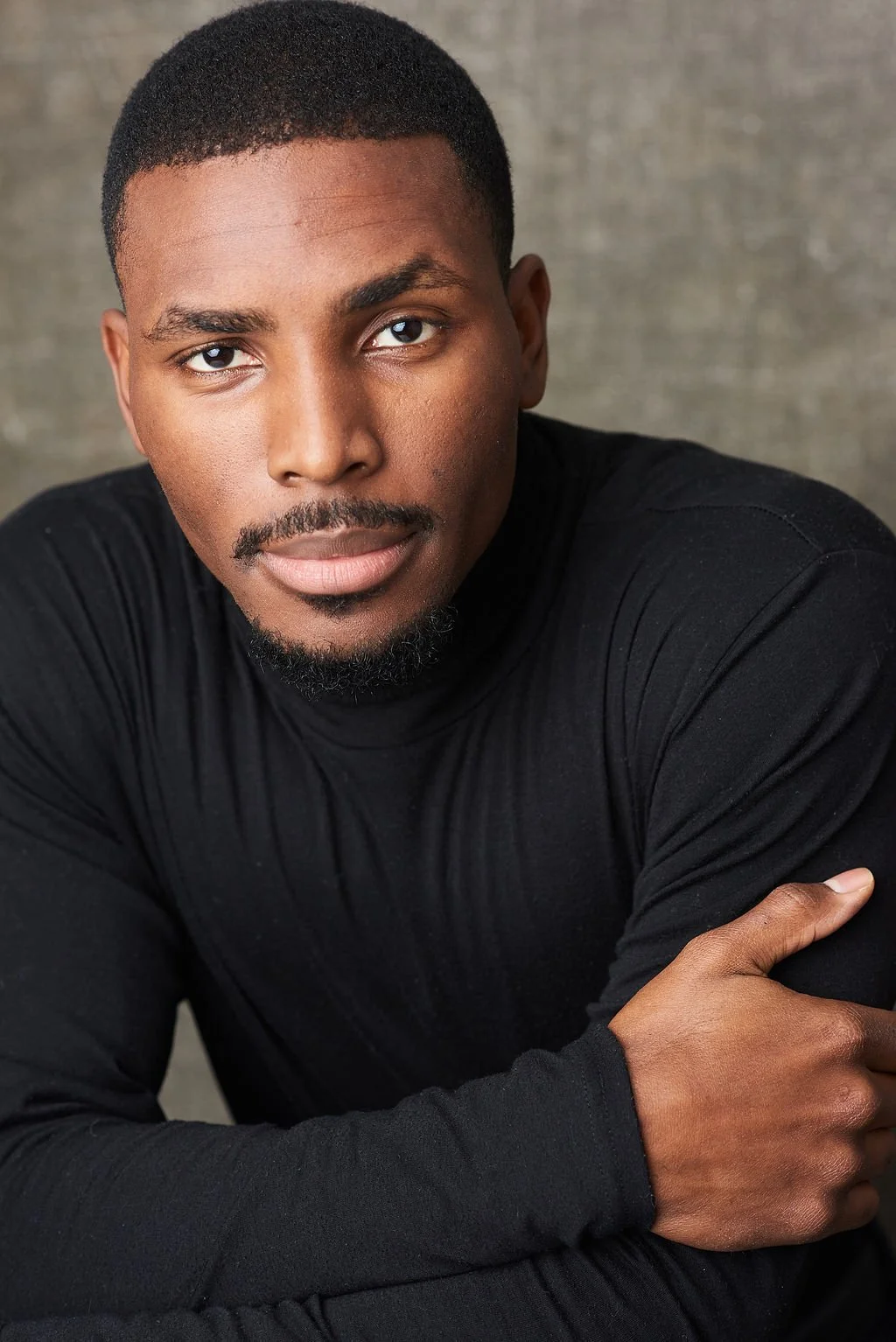 A young African American man with short hair and a goatee, wearing a black long-sleeve shirt, with a neutral background.