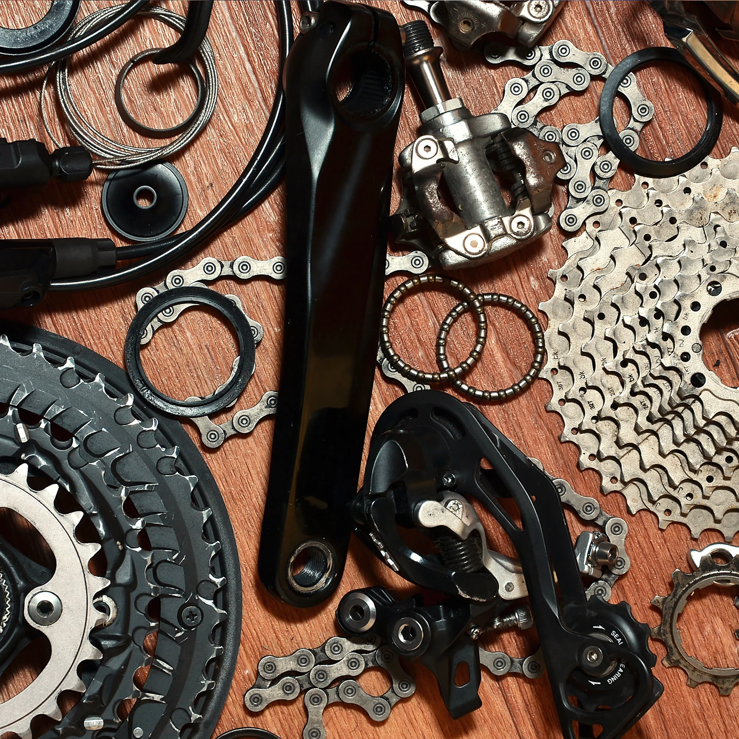 Collection of bicycle bike parts including chain, cogs, derailleur, chainring, cassette, and other small components on a wooden surface.