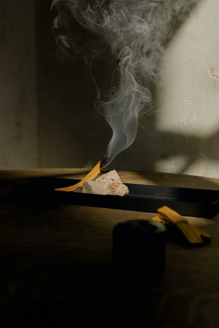 A lit matchstick resting on a small rock, producing smoke, with a black object and yellow item in the foreground.