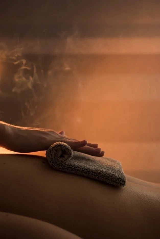 A person is receiving a massage with a rolled towel on their back in a dimly lit room with warm lighting.