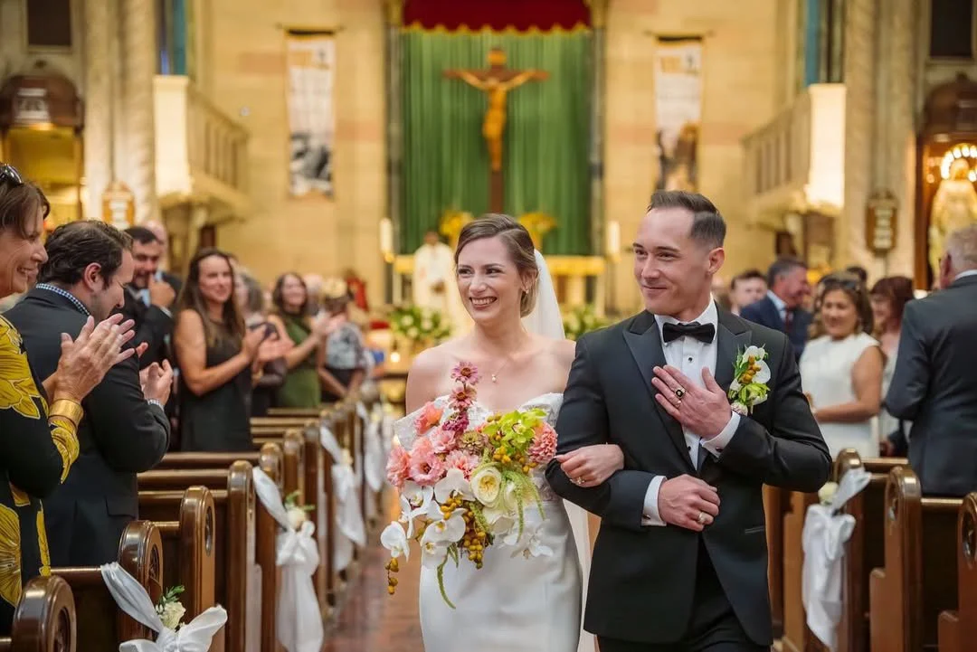 Bride and groom walking down the aisle after their wedding ceremony in a church, surrounded by clapping guests.
