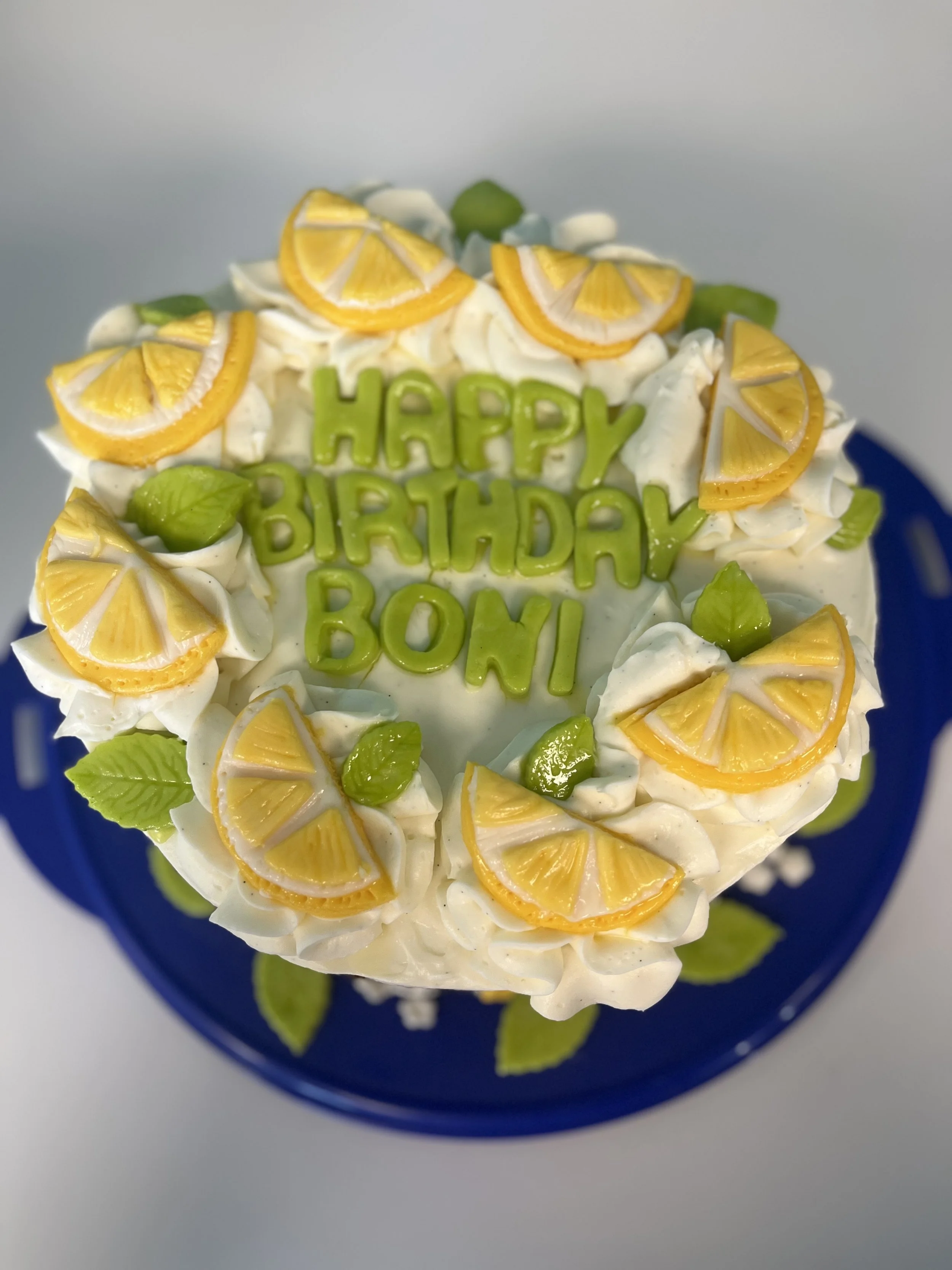 A birthday cake decorated with lemon slices and green leaves, with green letters spelling 'HAPPY BIRTHDAY BONI' on top.