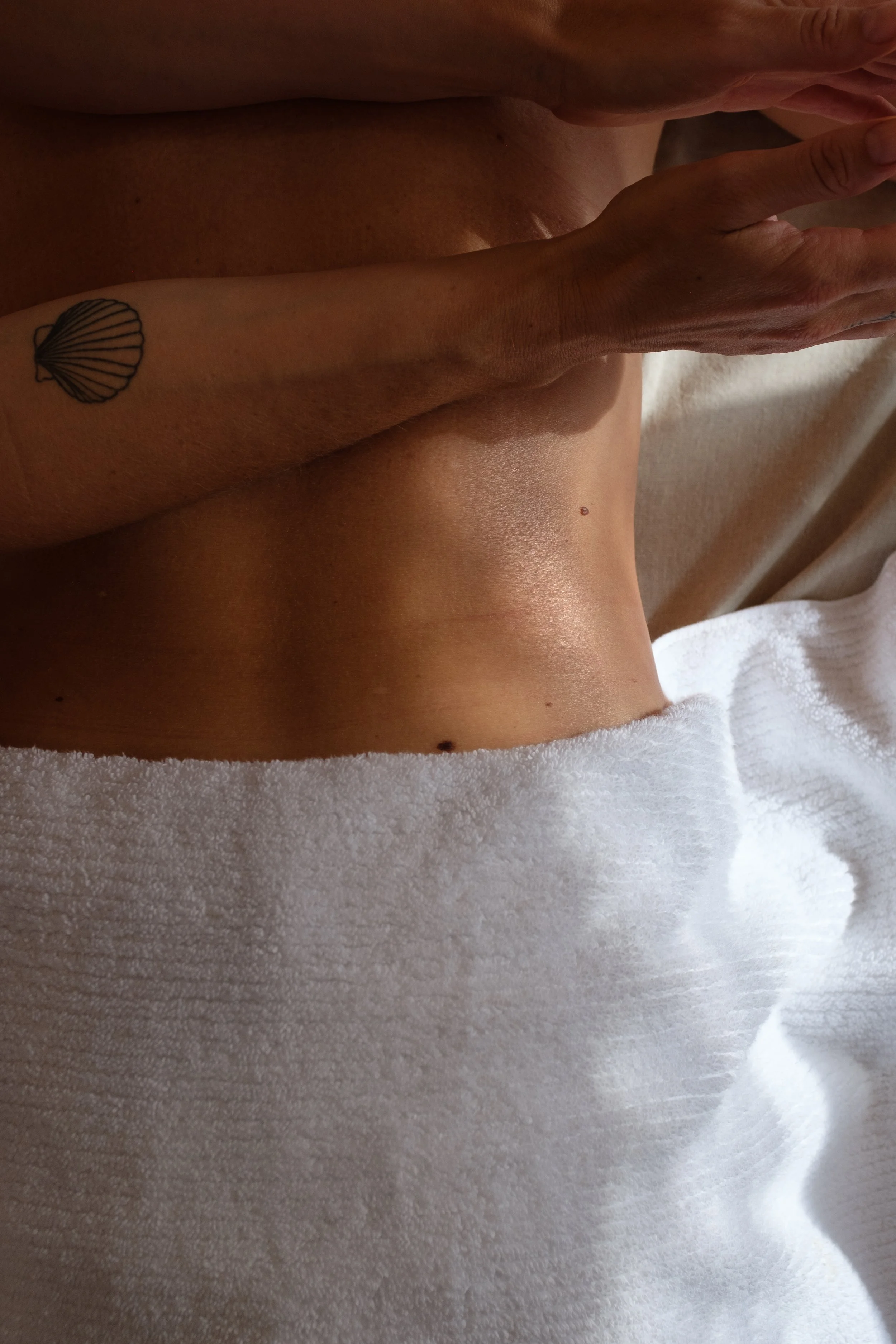 Close-up of a person's torso with a shell tattoo on the forearm, lying on a white towel.