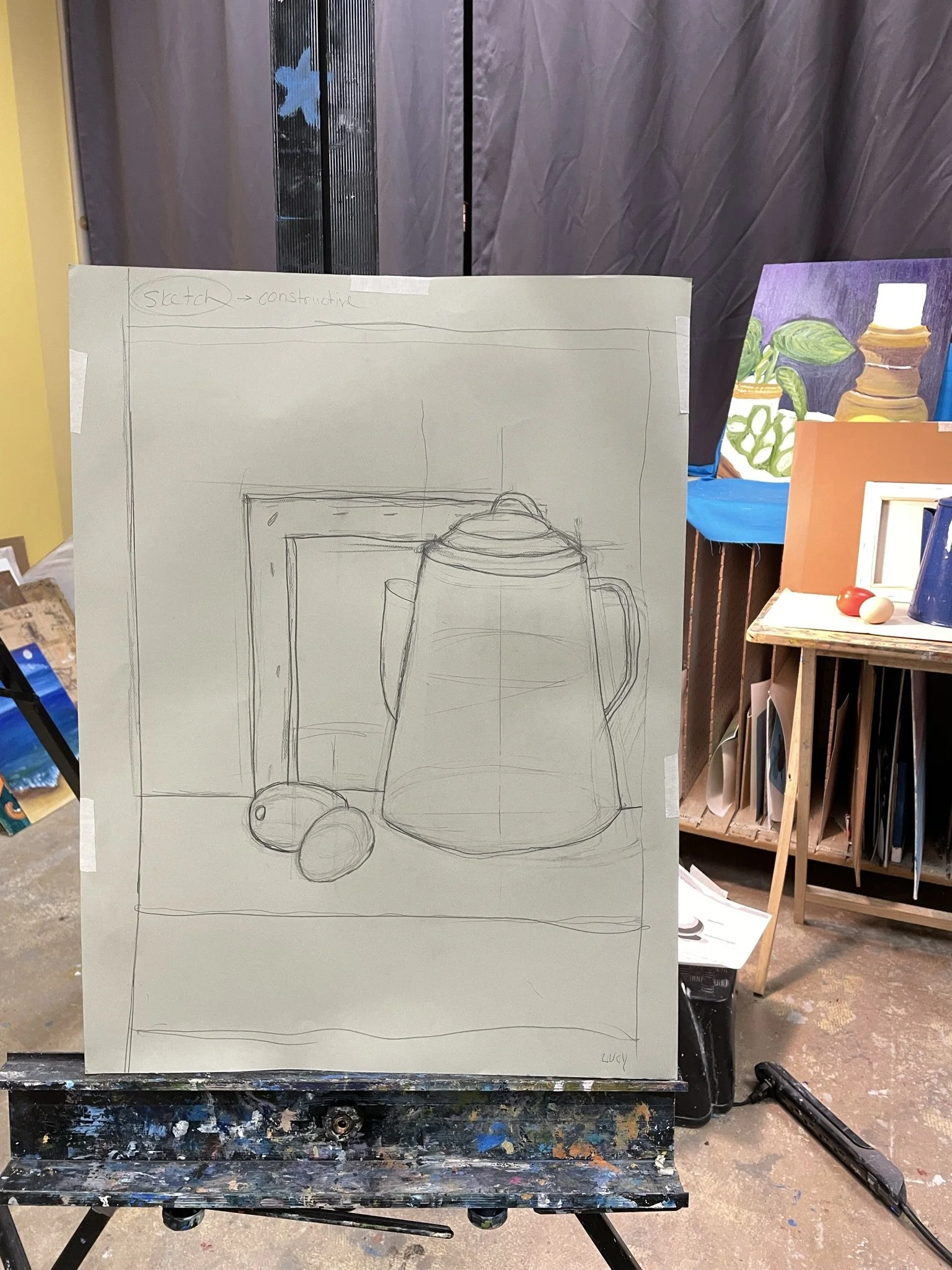 A finished sketch of a still life composition featuring a teapot, a cup, and a couple of fruits in front of a picture frame, on a canvas or paper on an artist's easel in an art studio.